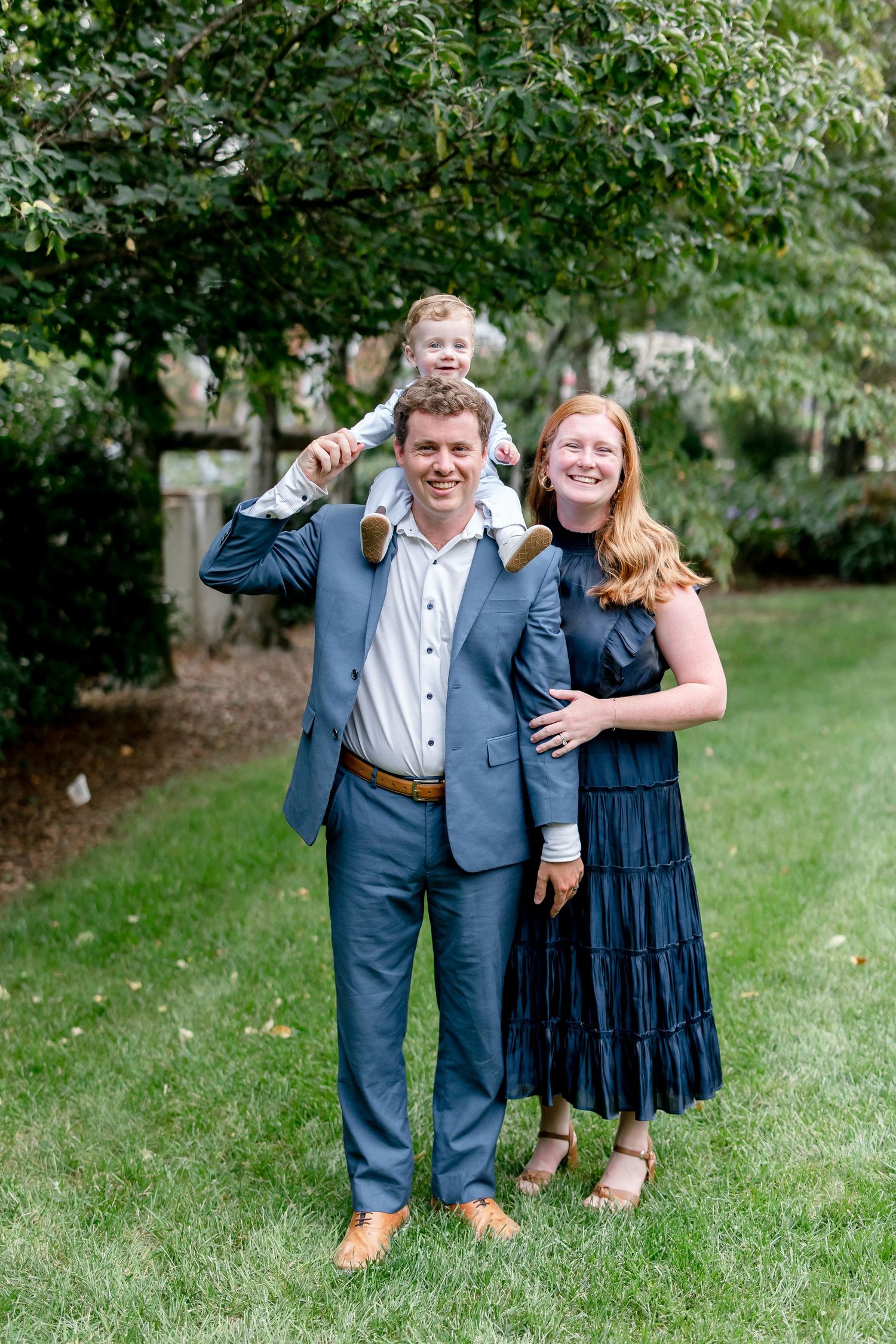 Couple poses outdoors in a garden setting wearing coordinated blue and navy formal attire.