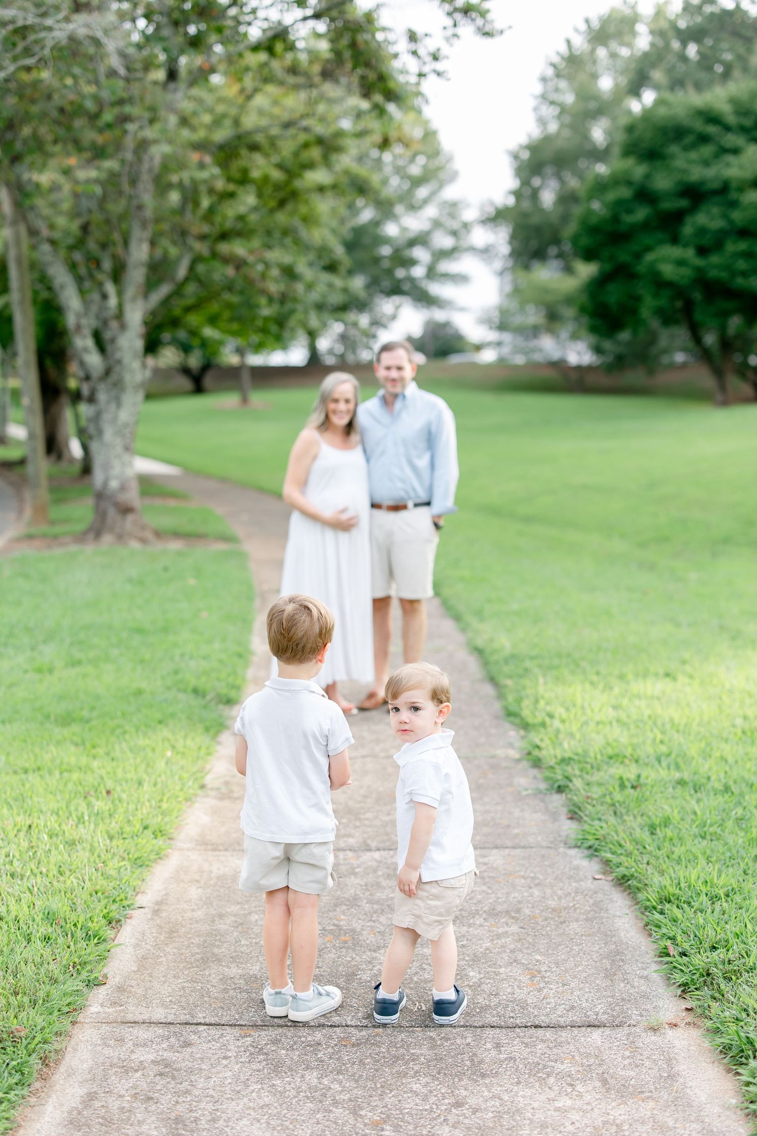 A family walks along a peaceful gravel path through a green park on a sunny day.