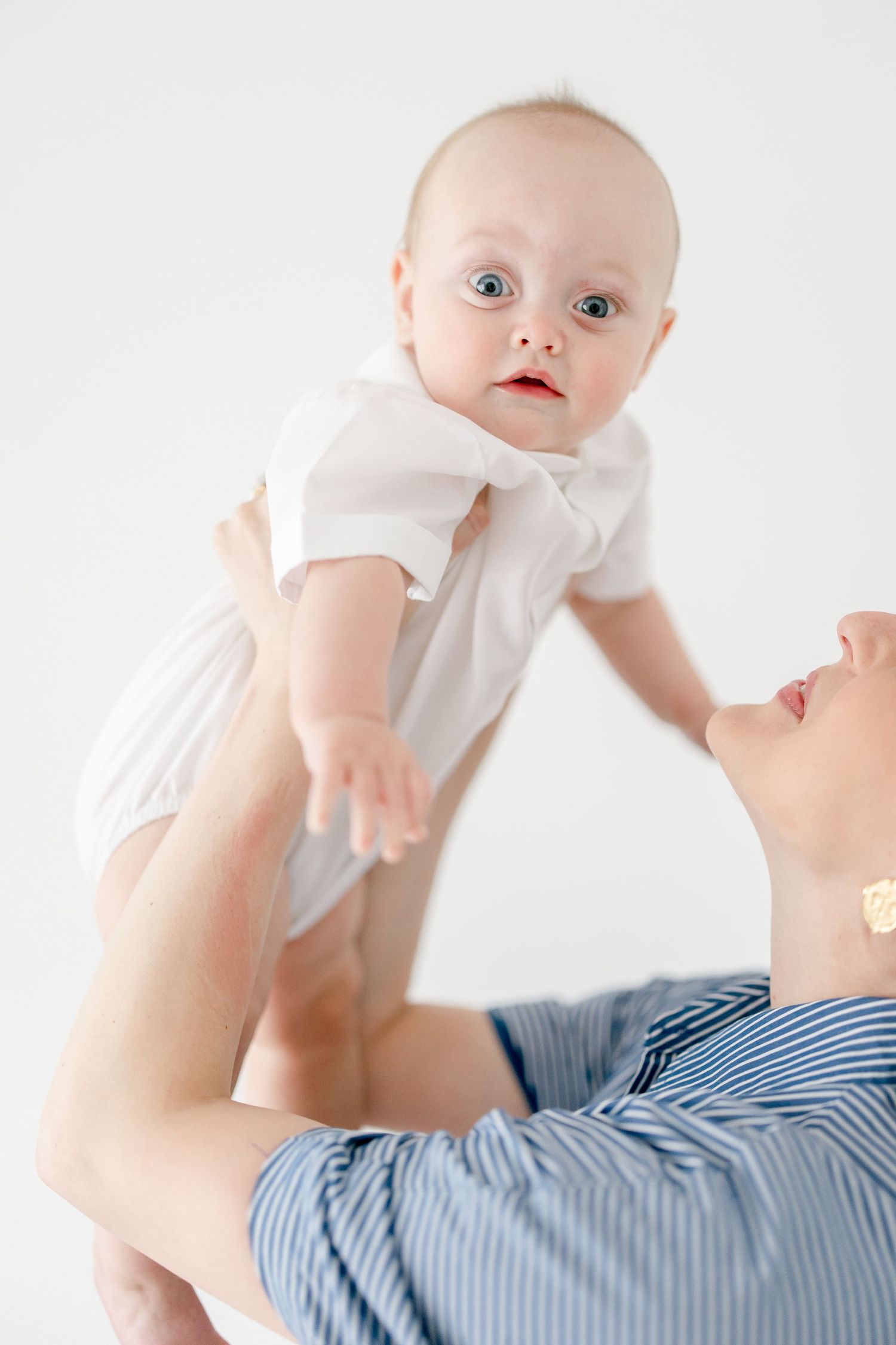 Baby wearing white lying on blue and white striped fabric against white background.