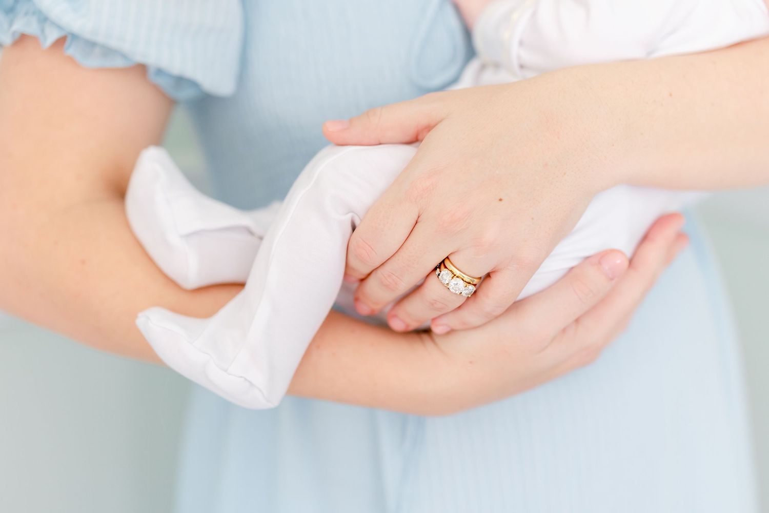 Close-up view of hands gently holding a soft white baby sock against a light blue background.