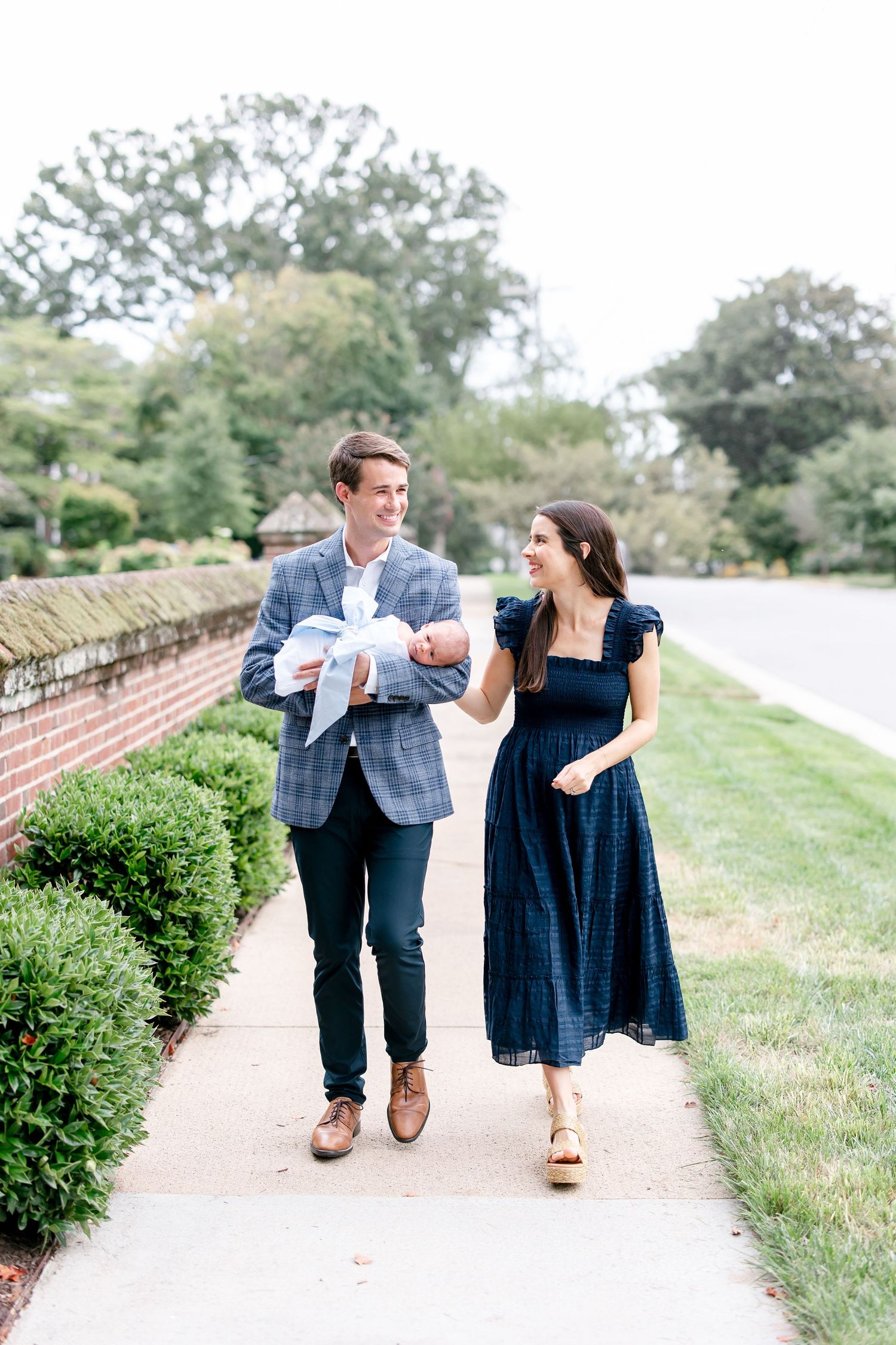 A couple in blue attire takes a romantic stroll along a brick-lined pathway surrounded by greenery.