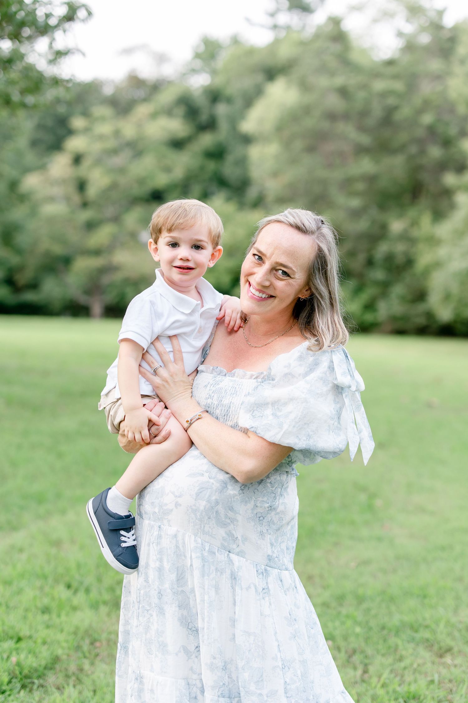 Joyful moments captured between parent and child in a light summer dress against greenery.