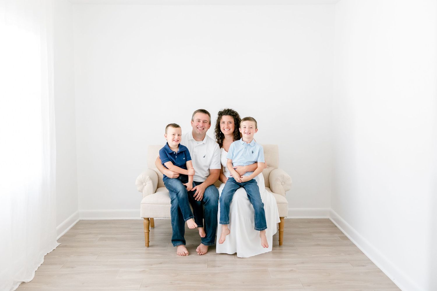 Family members in coordinated blue and white outfits sit together on a beige couch against white wall.