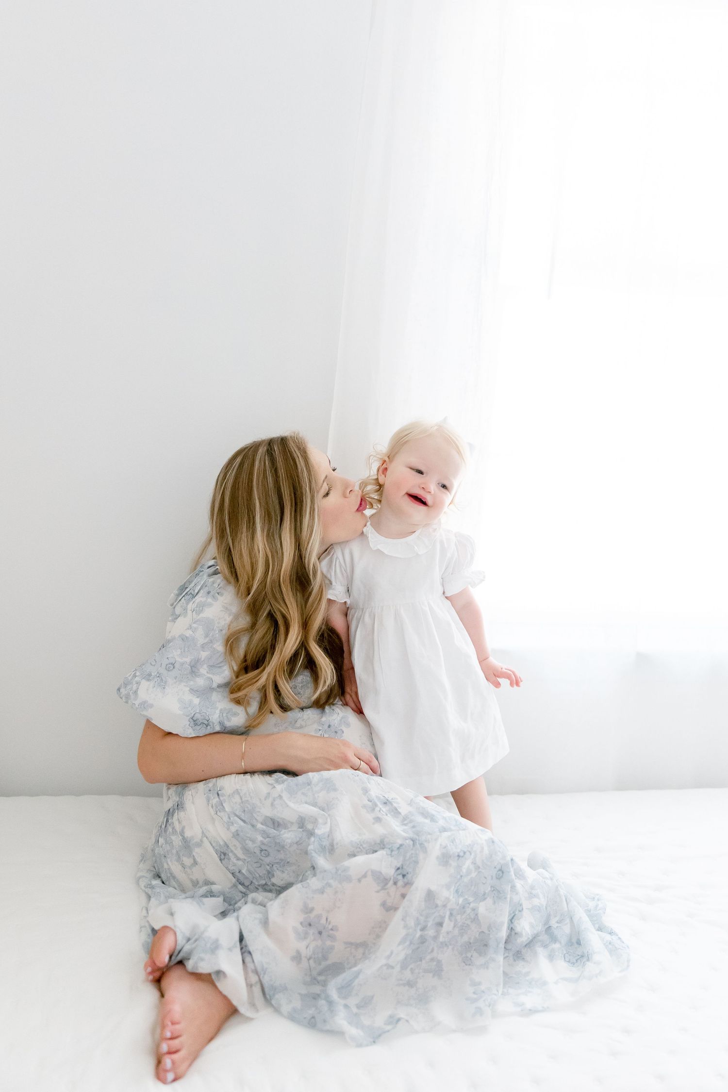Sweet maternity photoshoot series showing tender moments on a white backdrop wearing a soft blue floral dress.