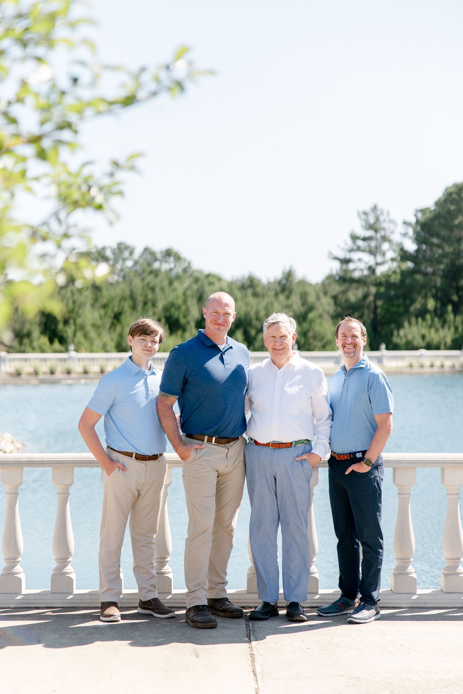 Four people wearing coordinated blue and white outfits pose together on a balcony with a lake view.