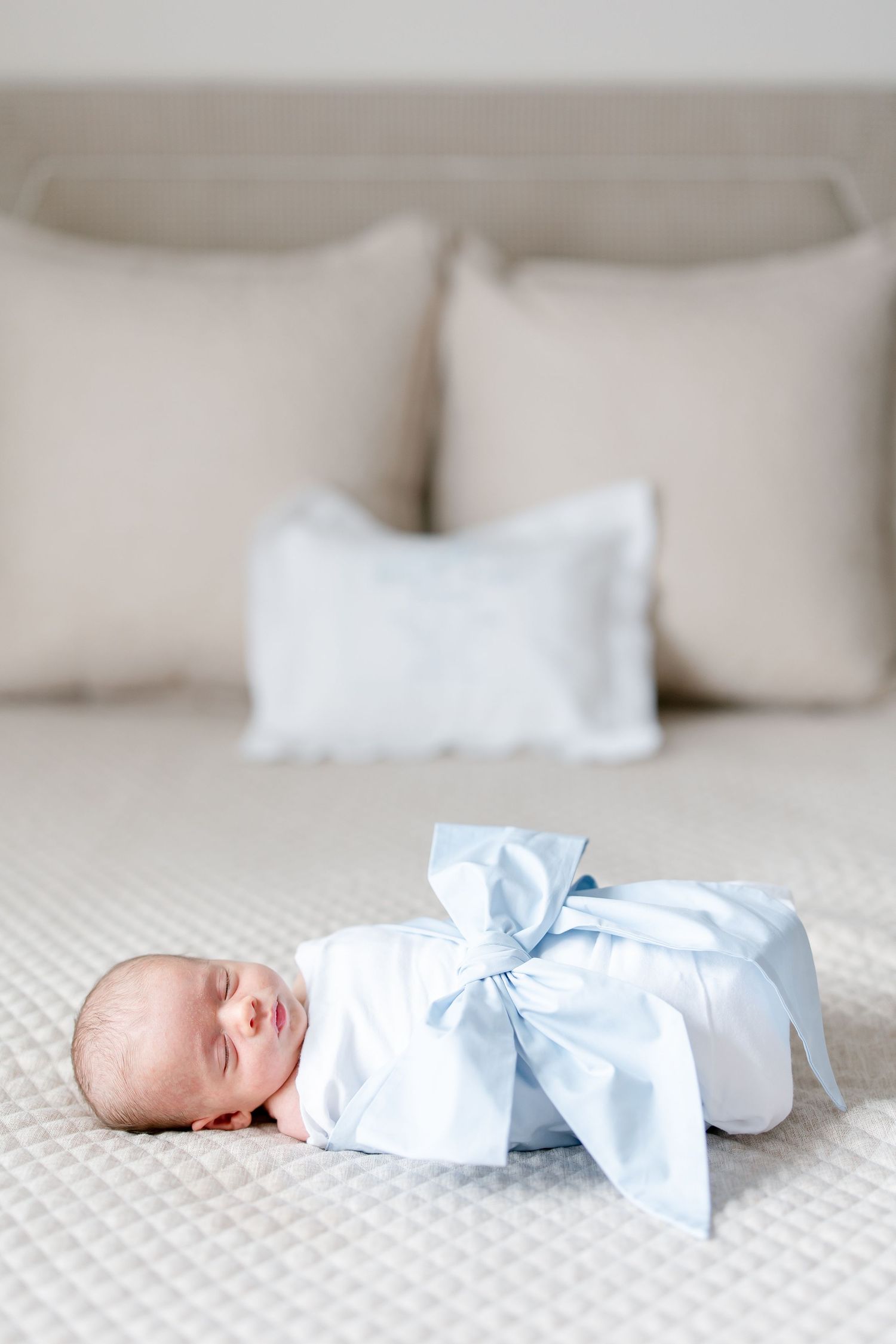 Baby in white swaddle lying on beige textured bedding in progressive stages.