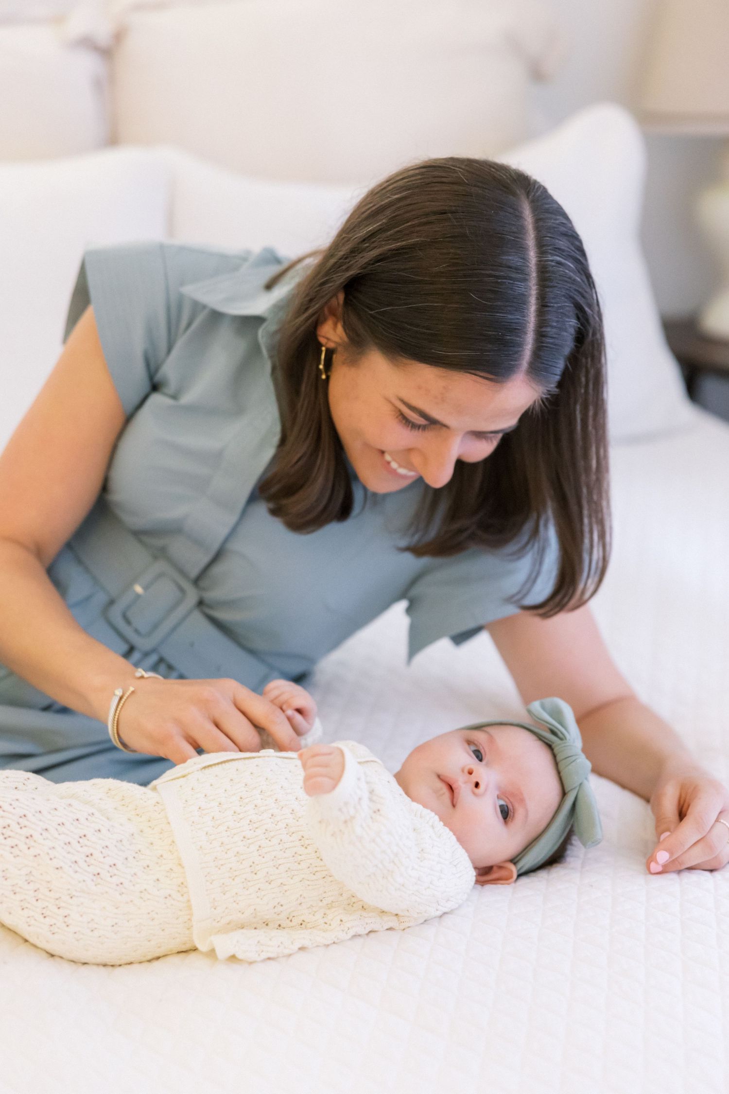 Parent tending to a peaceful sleeping baby swaddled in a polka dot blanket on a light colored surface.