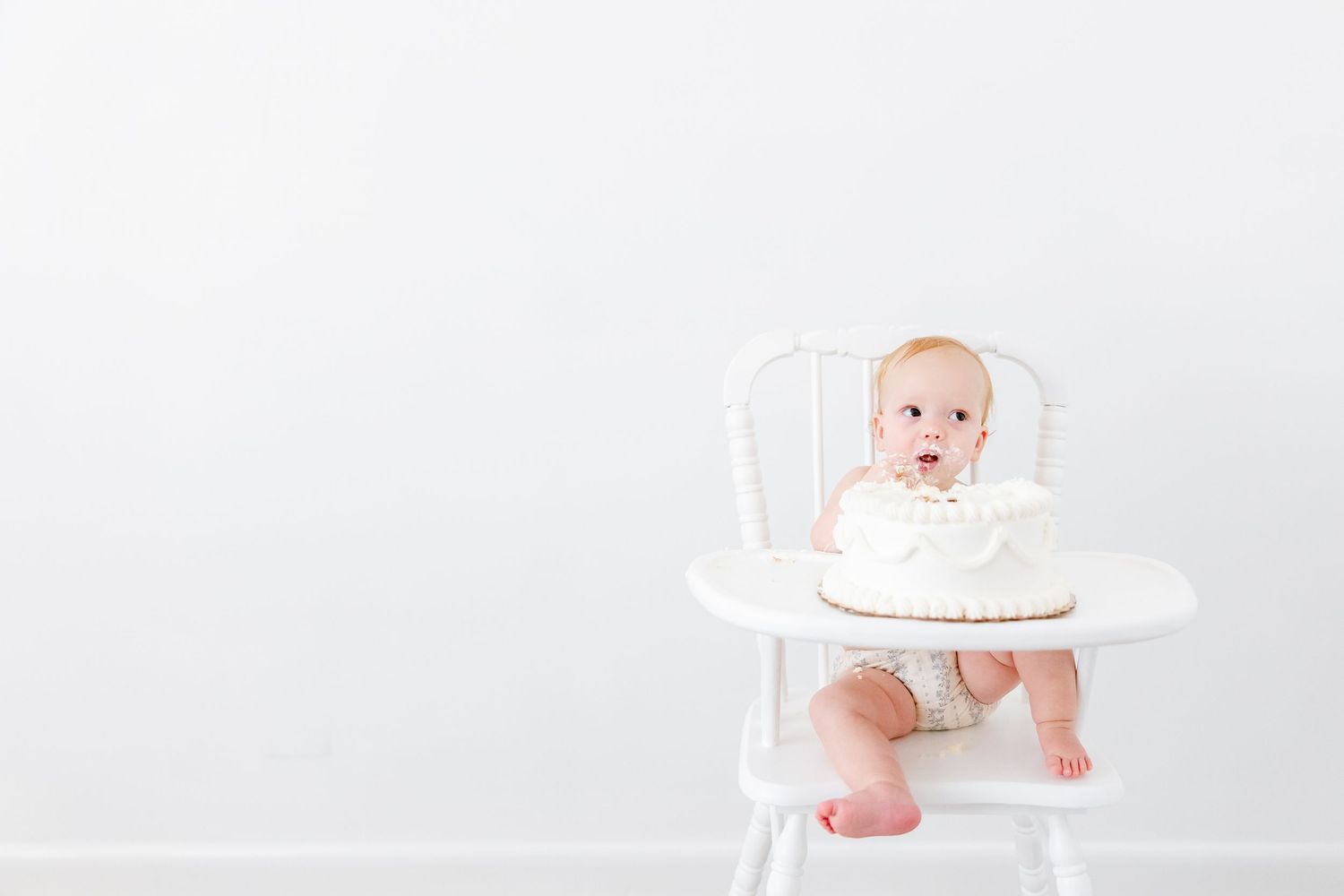 Baby sits in a classic white wooden high chair against a plain white background.