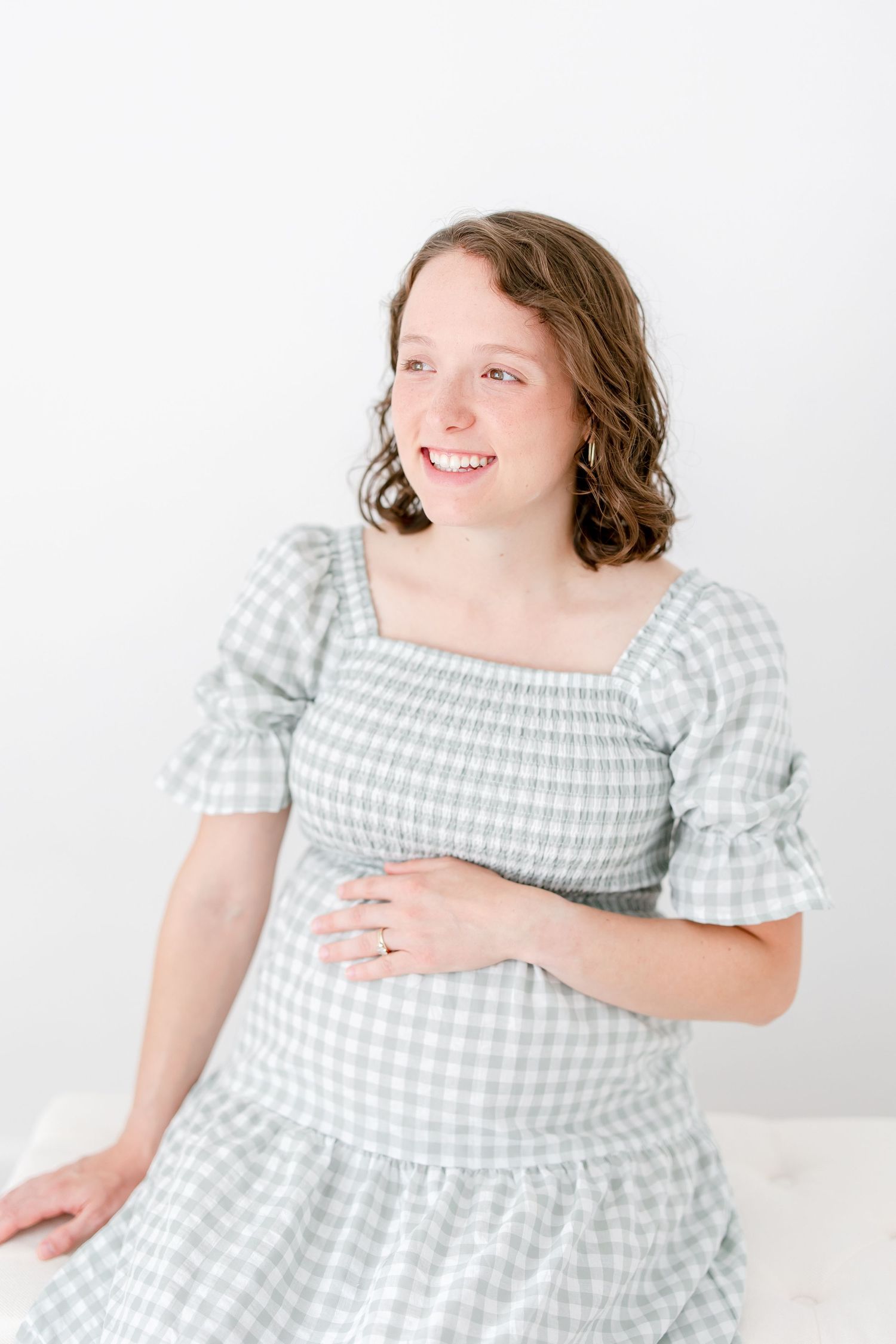 Cheerful person wearing a light green gingham check dress with puff sleeves poses against a white background.