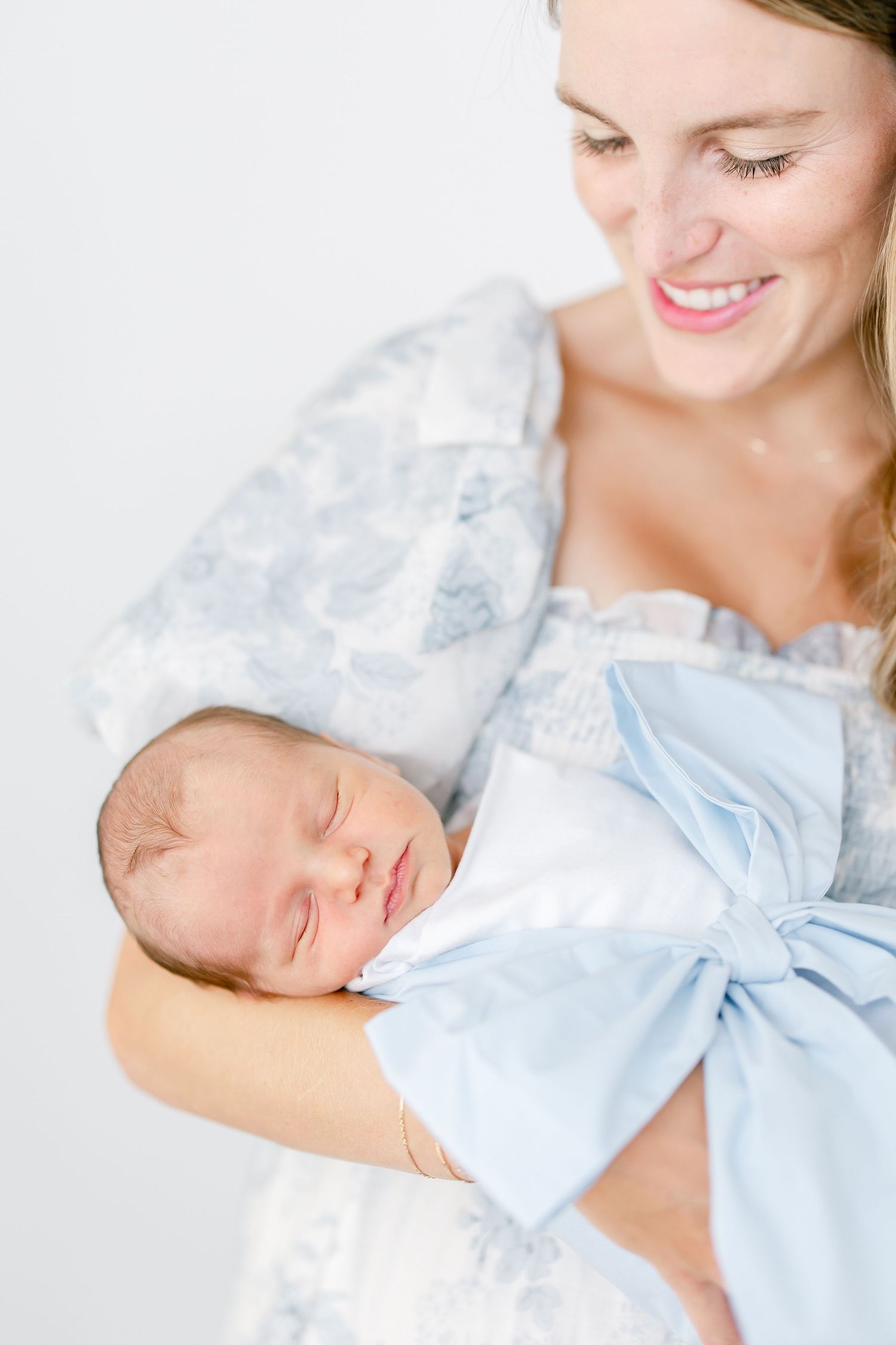 A series of tender images showing a mother in light blue clothing holding and gazing lovingly at her sleeping newborn baby.
