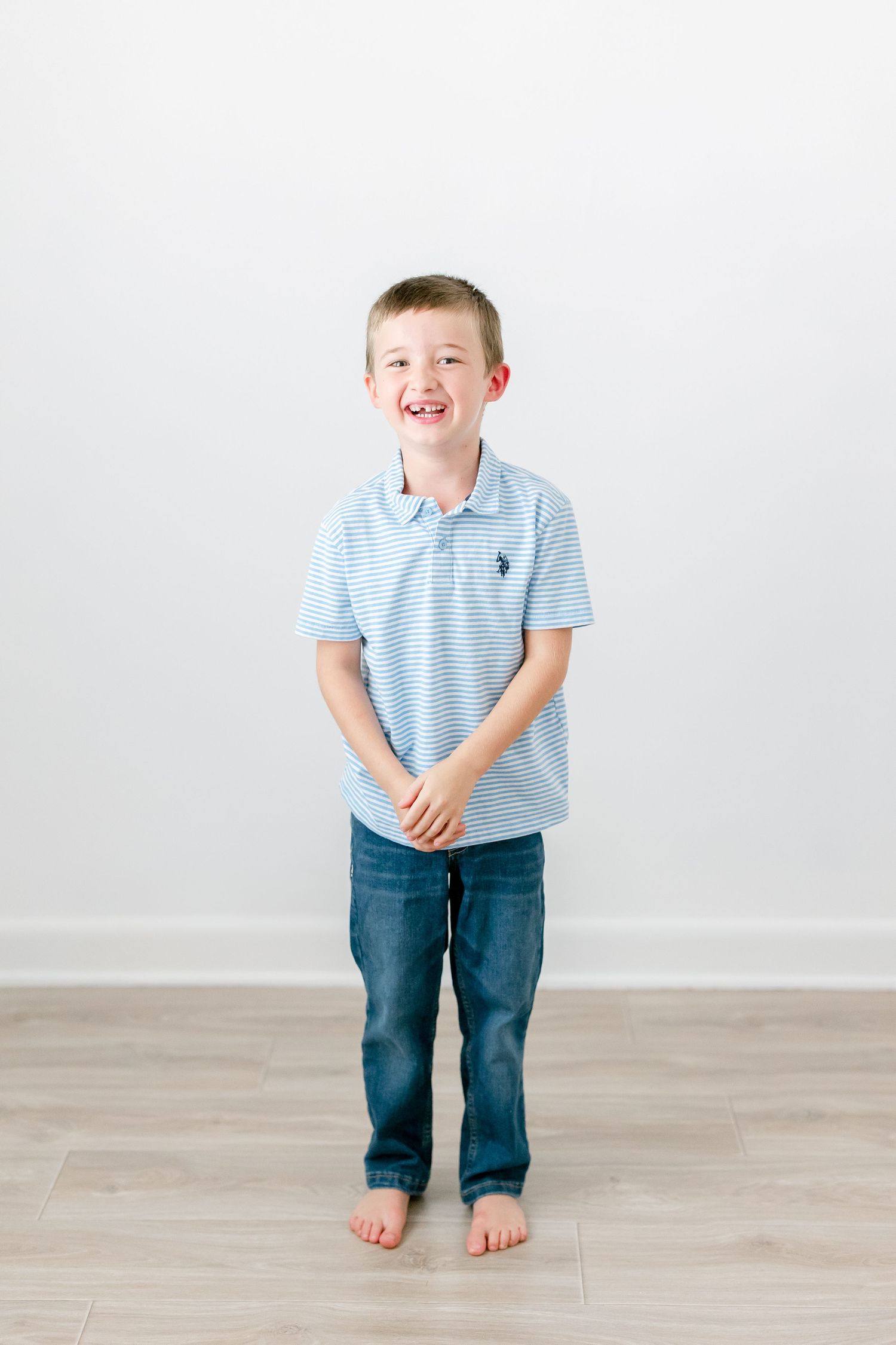 Young child in blue striped polo and jeans laughing while posing against white background.