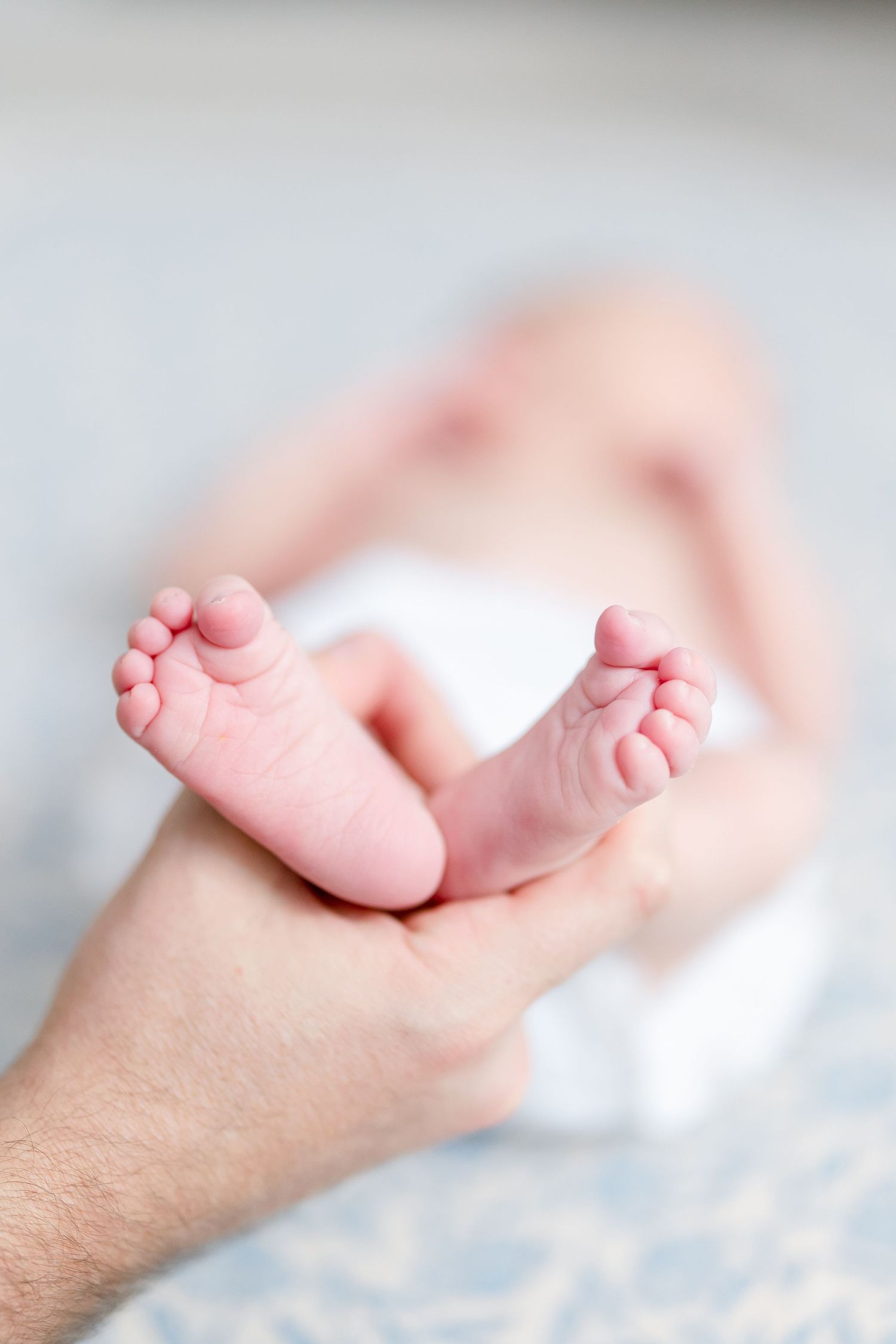 Tiny baby feet resting on an adult's arm against a light background, showing delicate toes and soft pink skin.