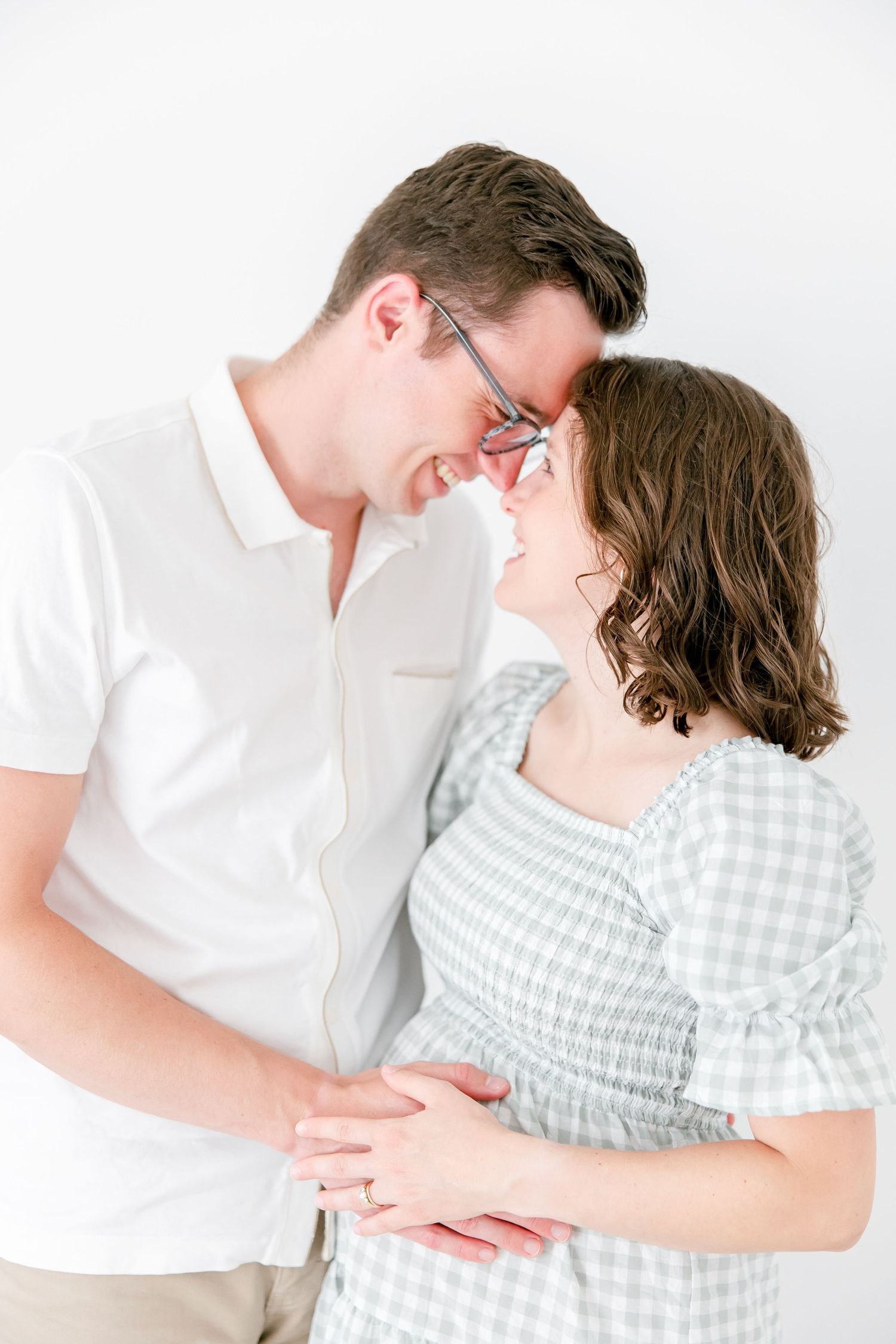 A couple in white and gingham embraces tenderly against a bright background, sharing an intimate moment together.