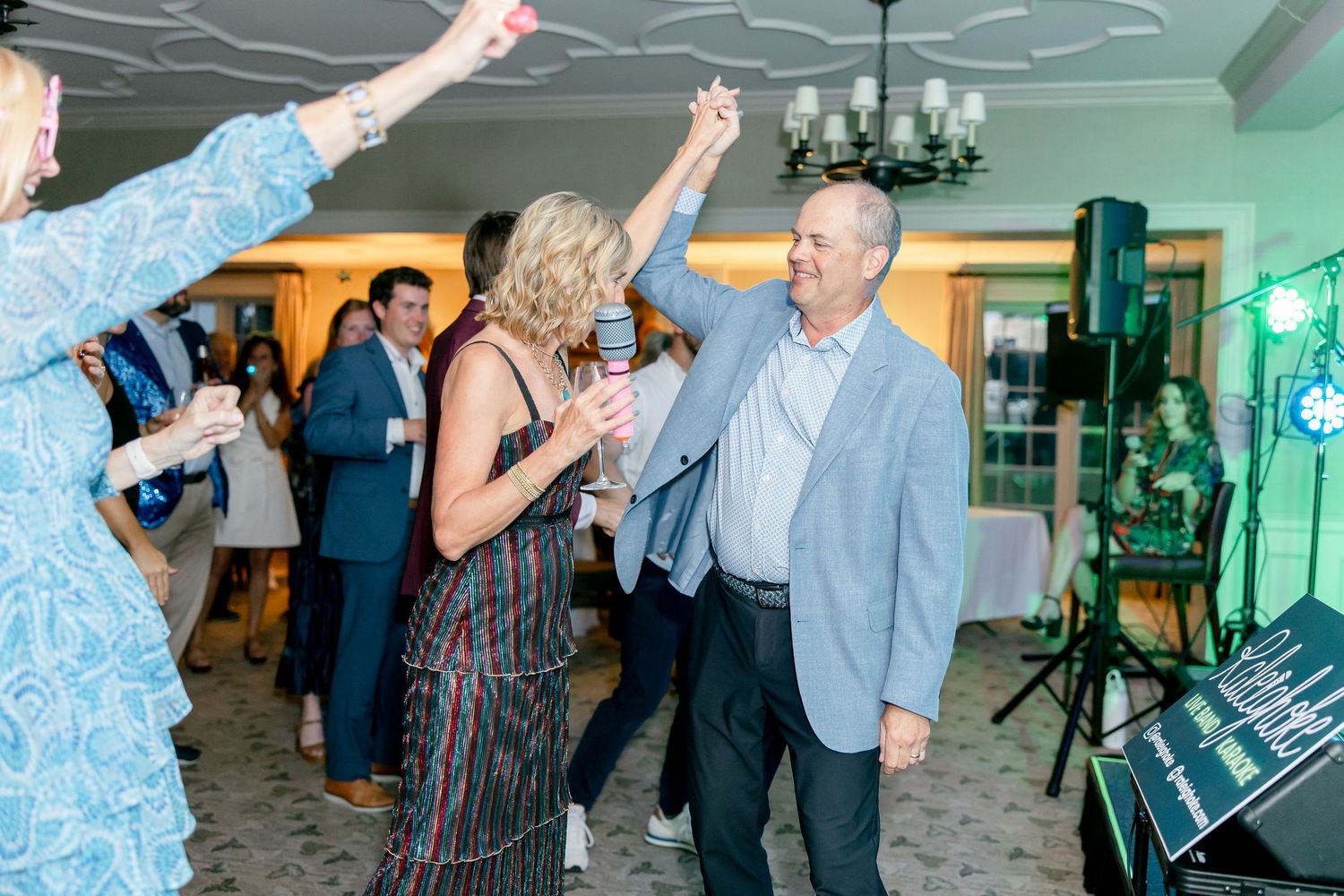 Group of people dancing and celebrating at a festive party with green lighting in an indoor venue.
