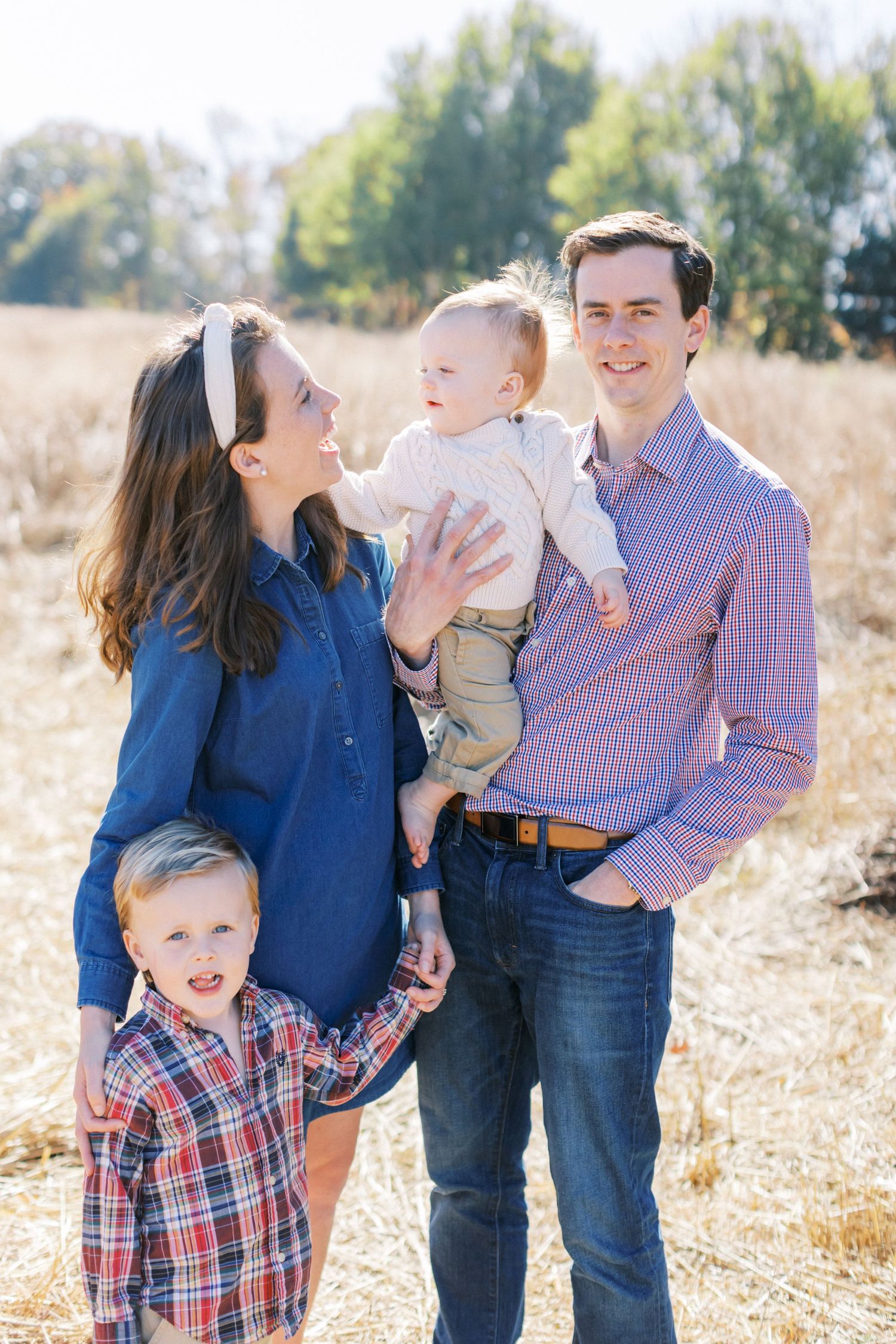 Family wearing pink and blue outfits laughs together during outdoor photo session in golden grass field.