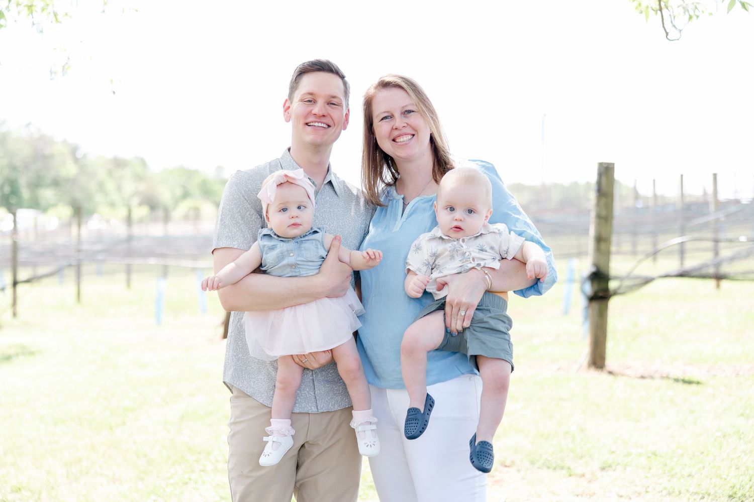 Family with twins posing outdoors on a sunny day in casual attire.
