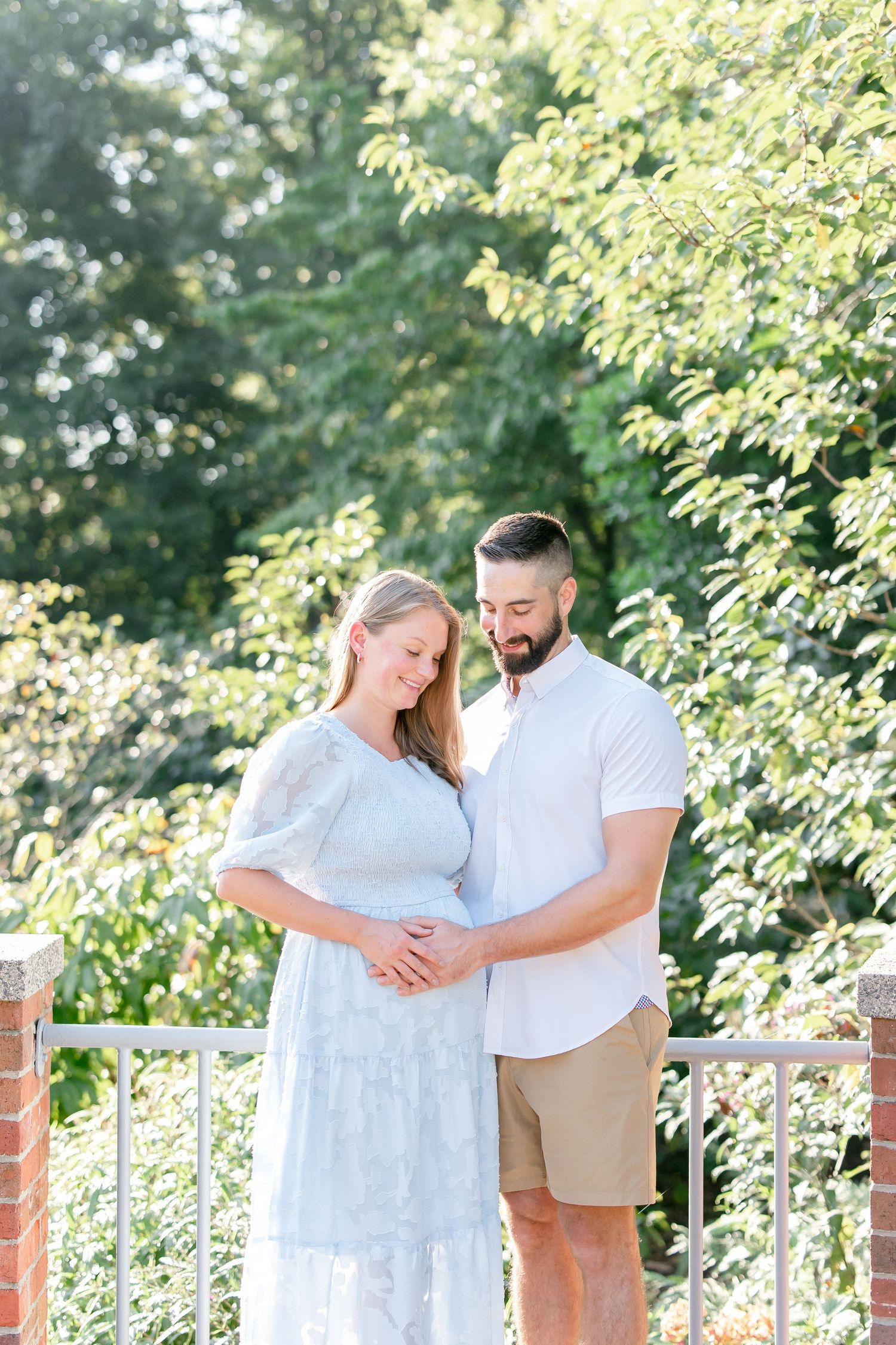 Sweet couple embracing on an outdoor deck with lush summer foliage in the background.