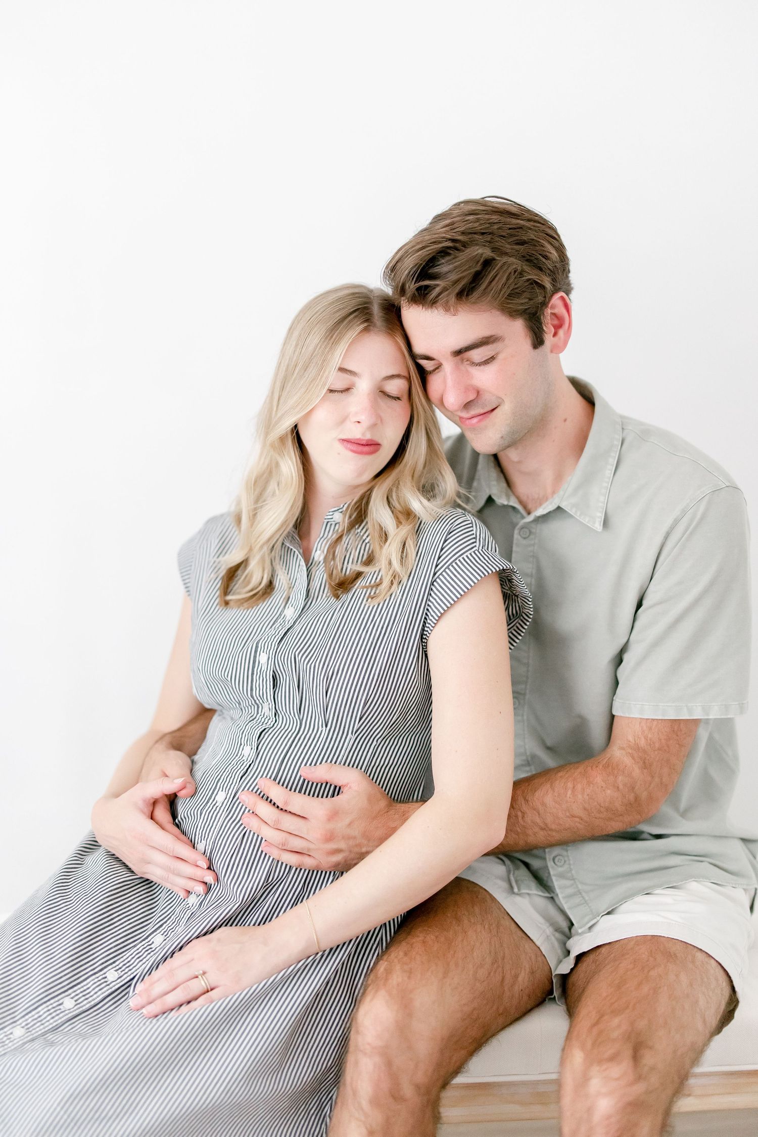 Intimate maternity portrait of couple in gray and white clothing on minimalist background.