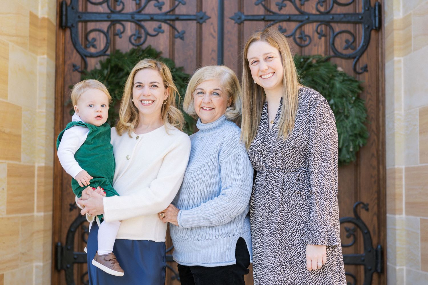 Multigenerational group poses together on front steps by ornate iron door with seasonal wreath decoration.