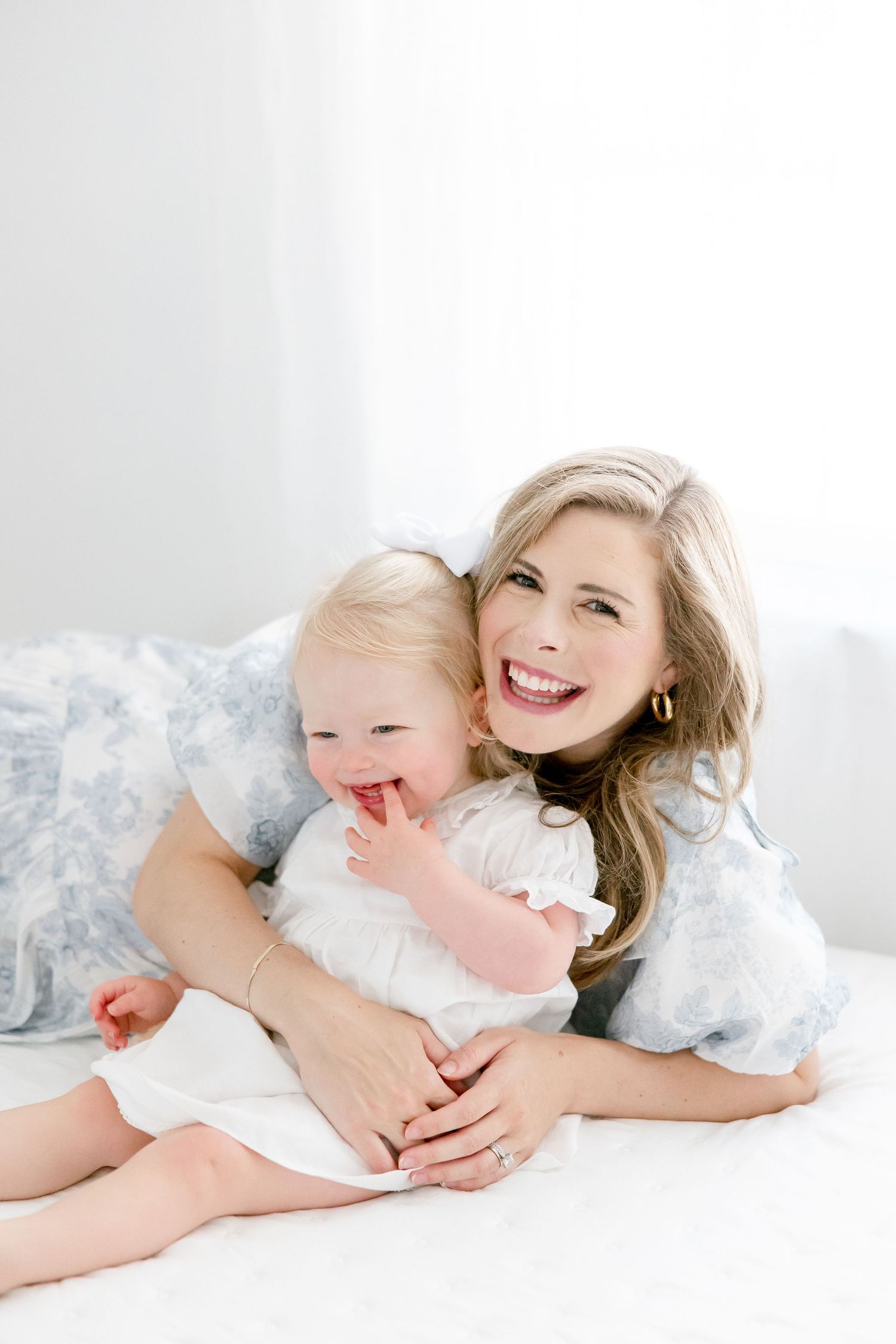 Parent and child sharing joyful affectionate moments while lying on white floor in casual attire.