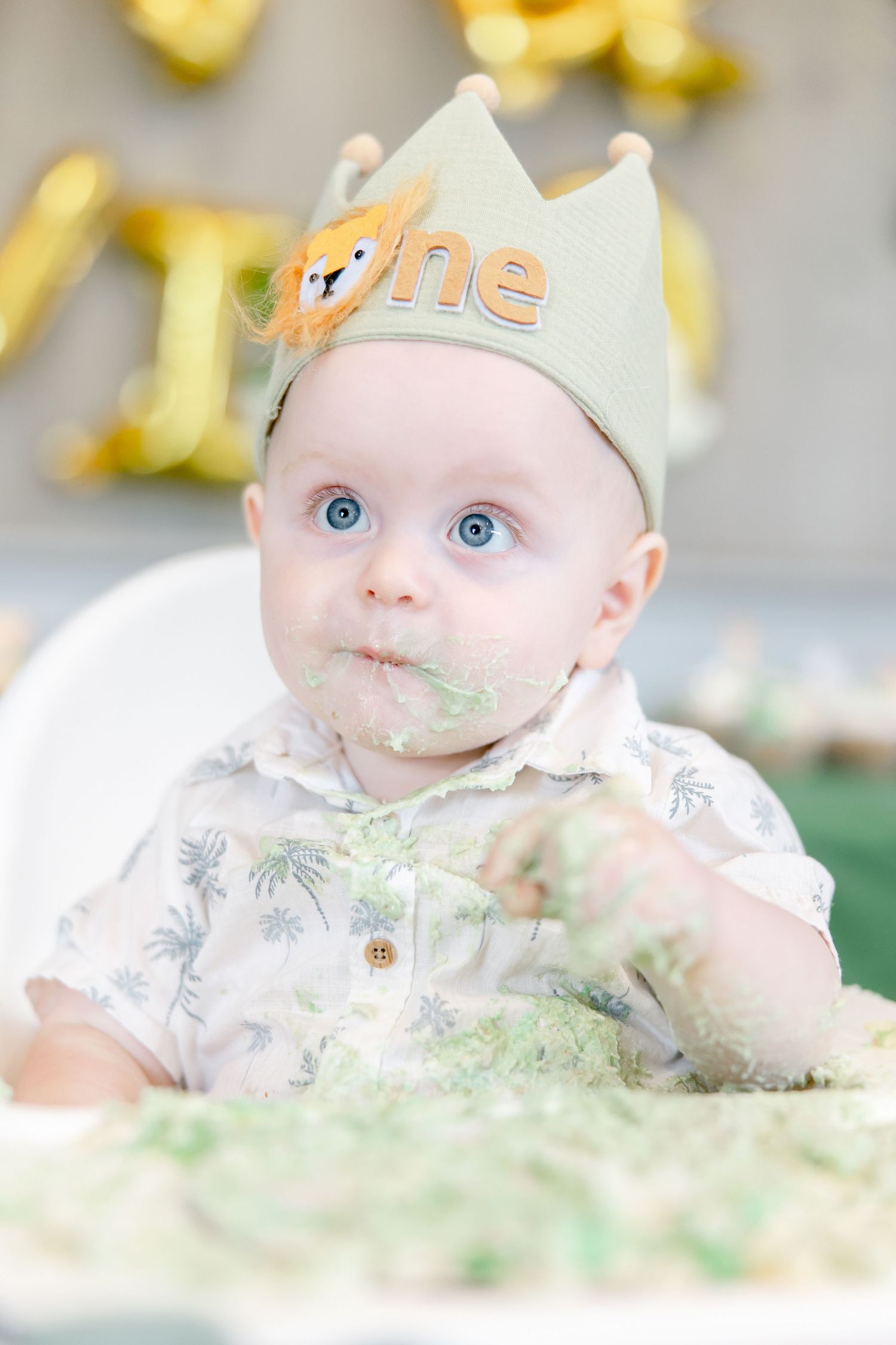 Baby in white outfit wearing crown with fox detail covered in green frosting.