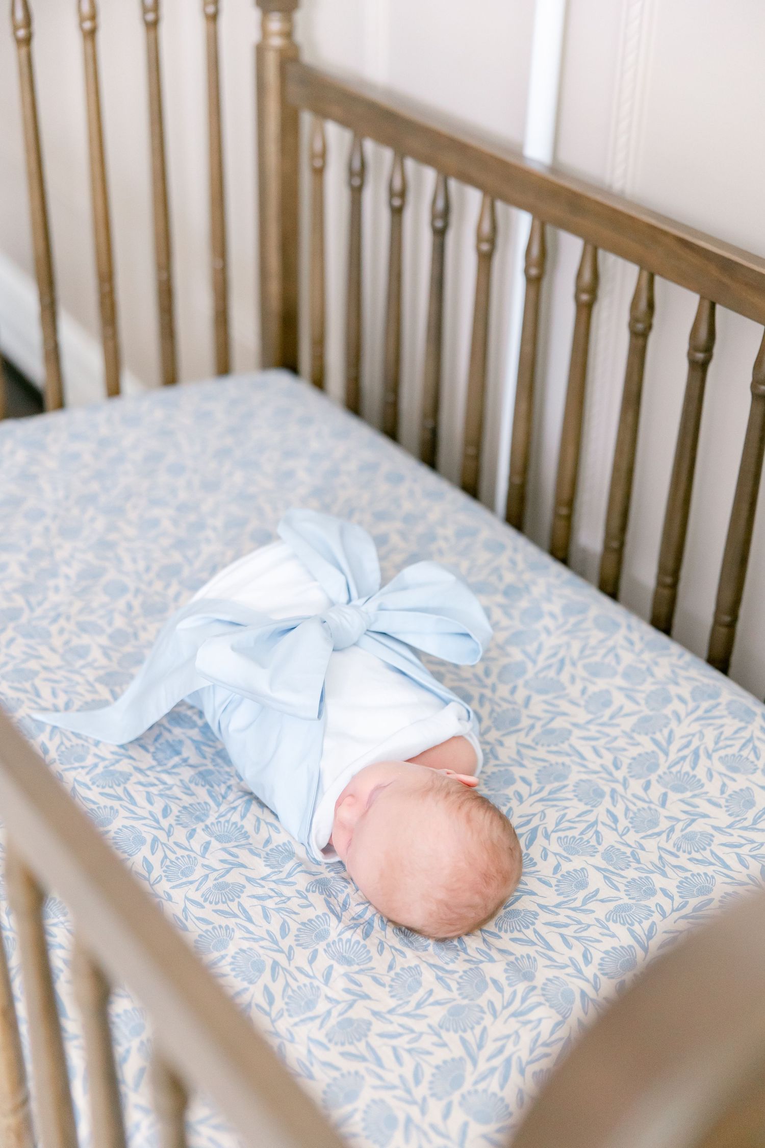 Baby crib with pale blue floral bedding and wooden spindles.