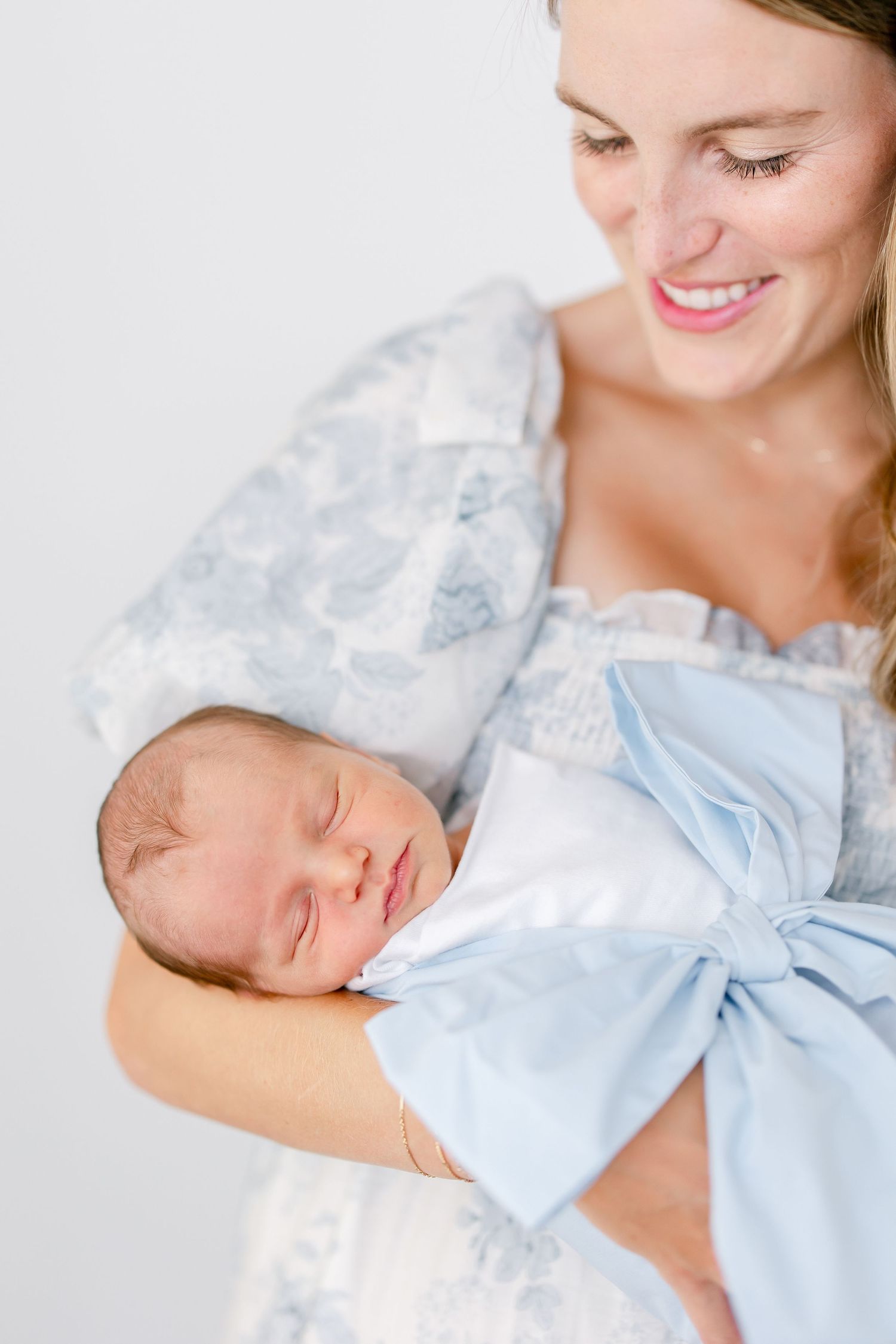 A sleeping newborn baby in light blue clothing is held tenderly against someone's chest.