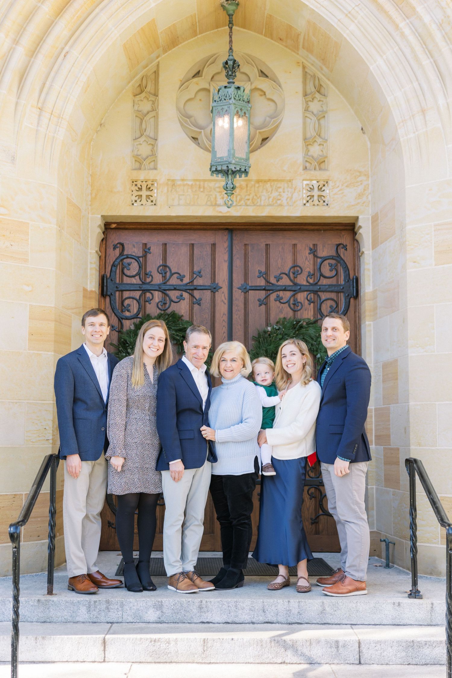 A professionally dressed group stands on stone church steps in front of an ornate wooden door and vintage lantern.