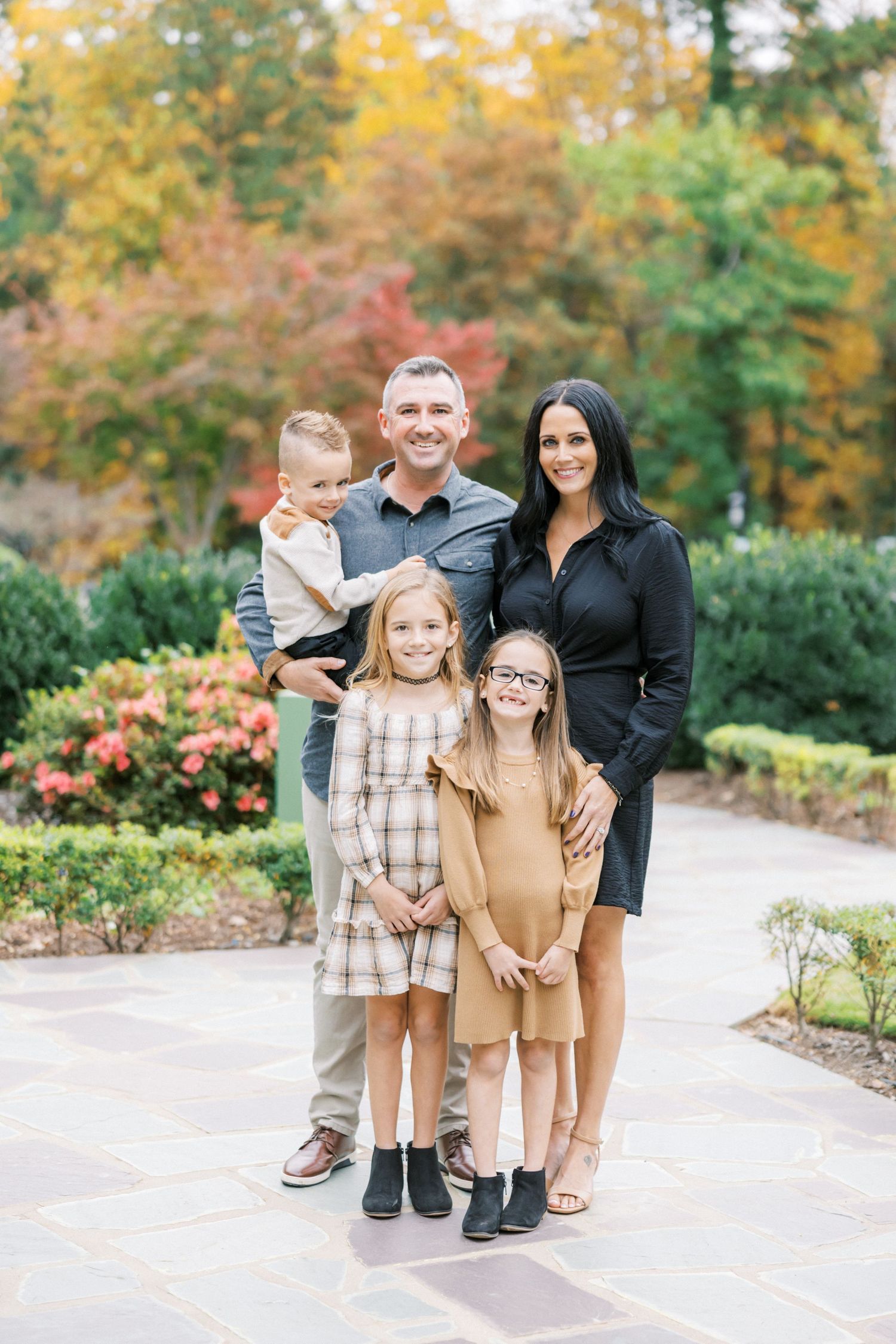 A family poses together on a stone path surrounded by vibrant fall foliage and garden landscaping.