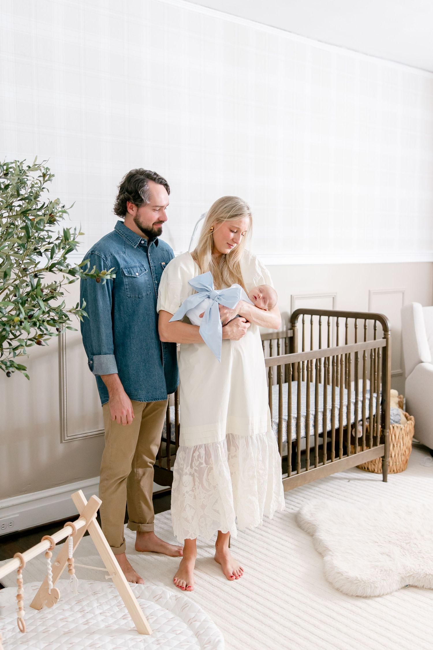 A couple dancing together in a bright white nursery room with a wooden crib and plush rug.