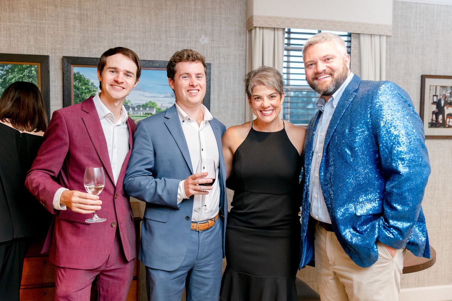 A group of well-dressed individuals pose at a formal event, with one wearing a burgundy suit and another in a blue sequined jacket.
