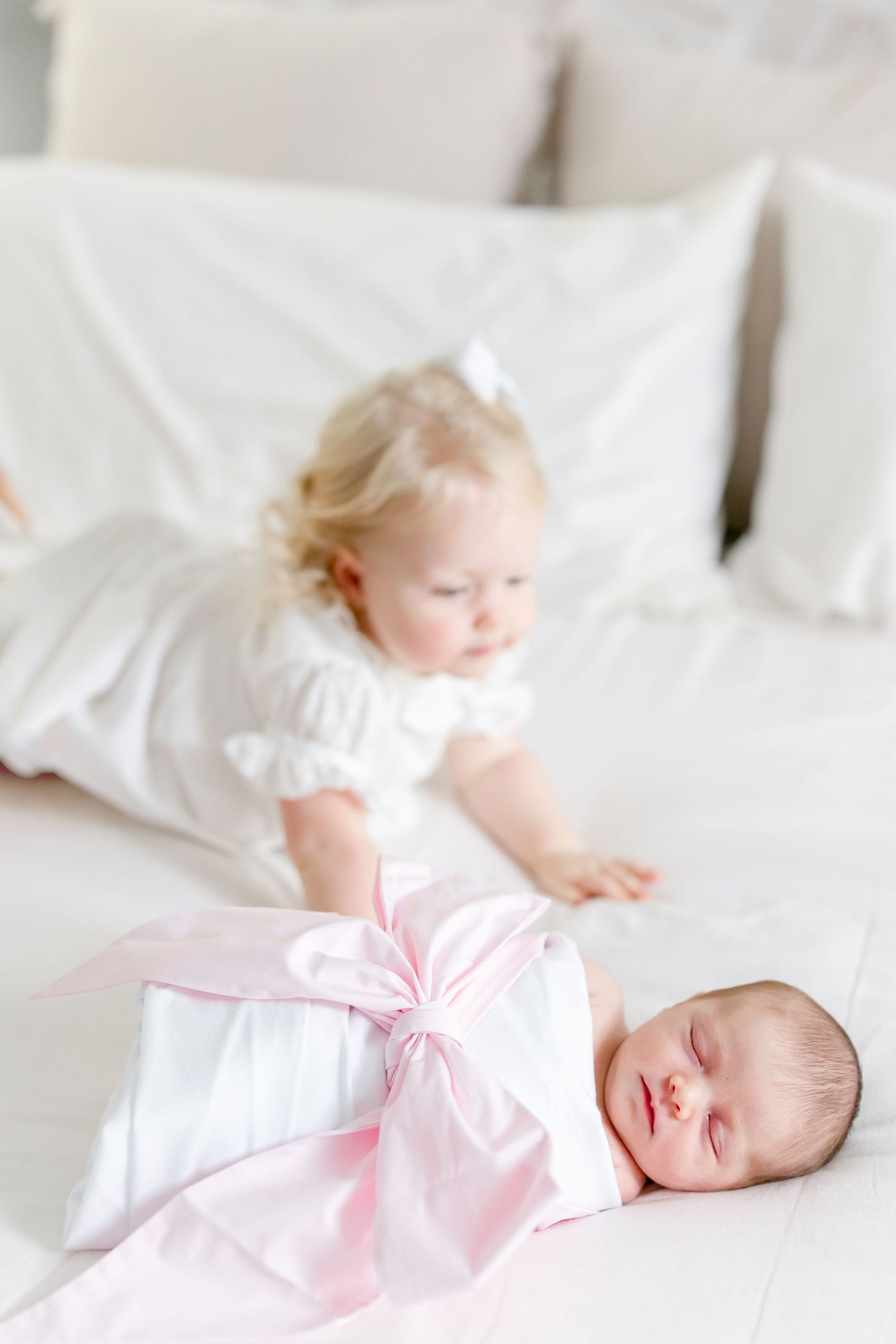 Sleeping baby in pink outfit rests peacefully on white bedding.
