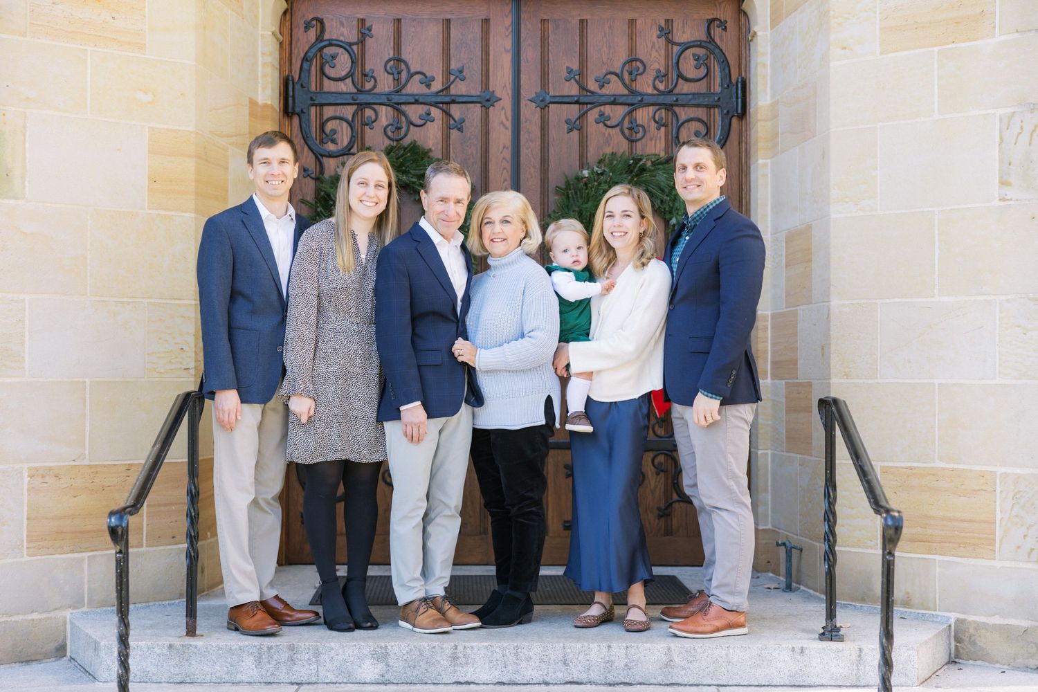 A group of people dressed in business casual attire stand together on stone steps in front of an ornate iron door.