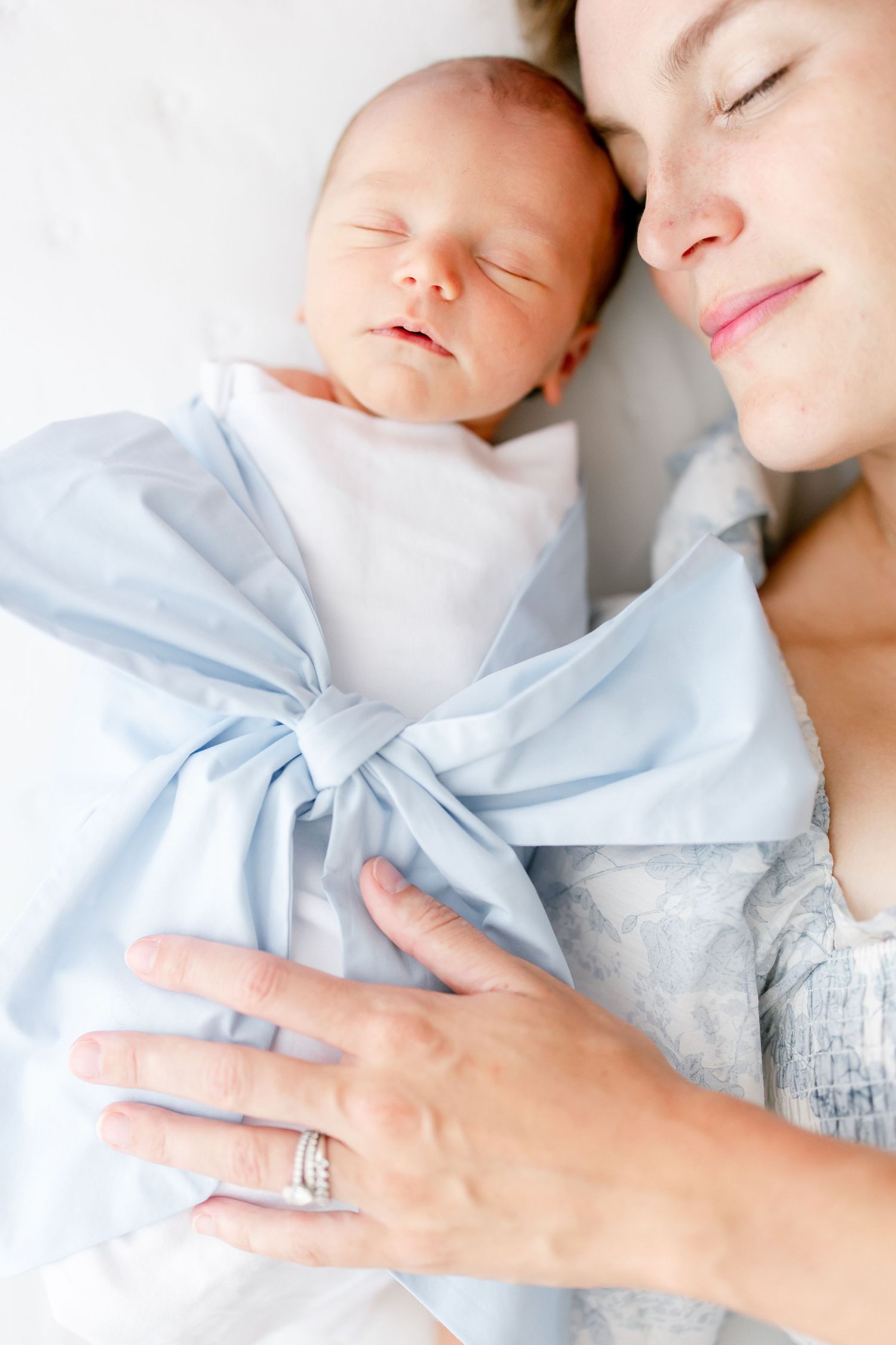 A sleeping newborn baby swaddled in light blue fabric rests peacefully next to parent in tender moment.