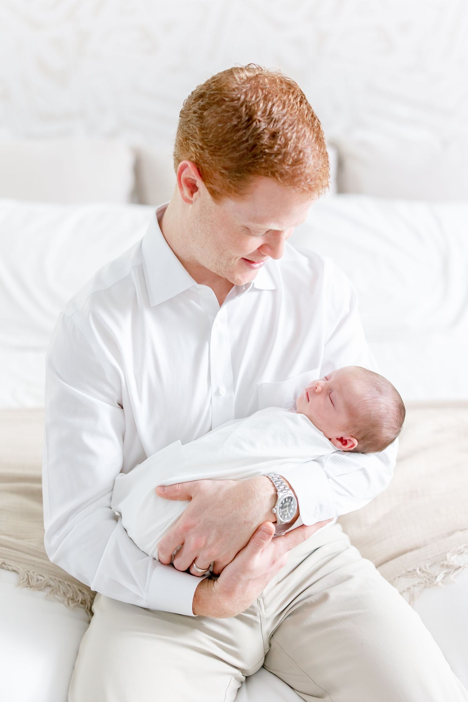 Parent wearing white shirt cradles sleeping newborn on white bedding.