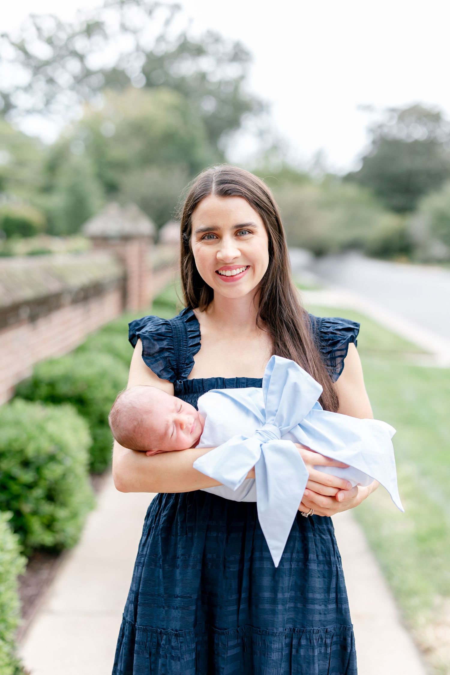 Woman in navy dress poses with newborn on brick-lined garden path.