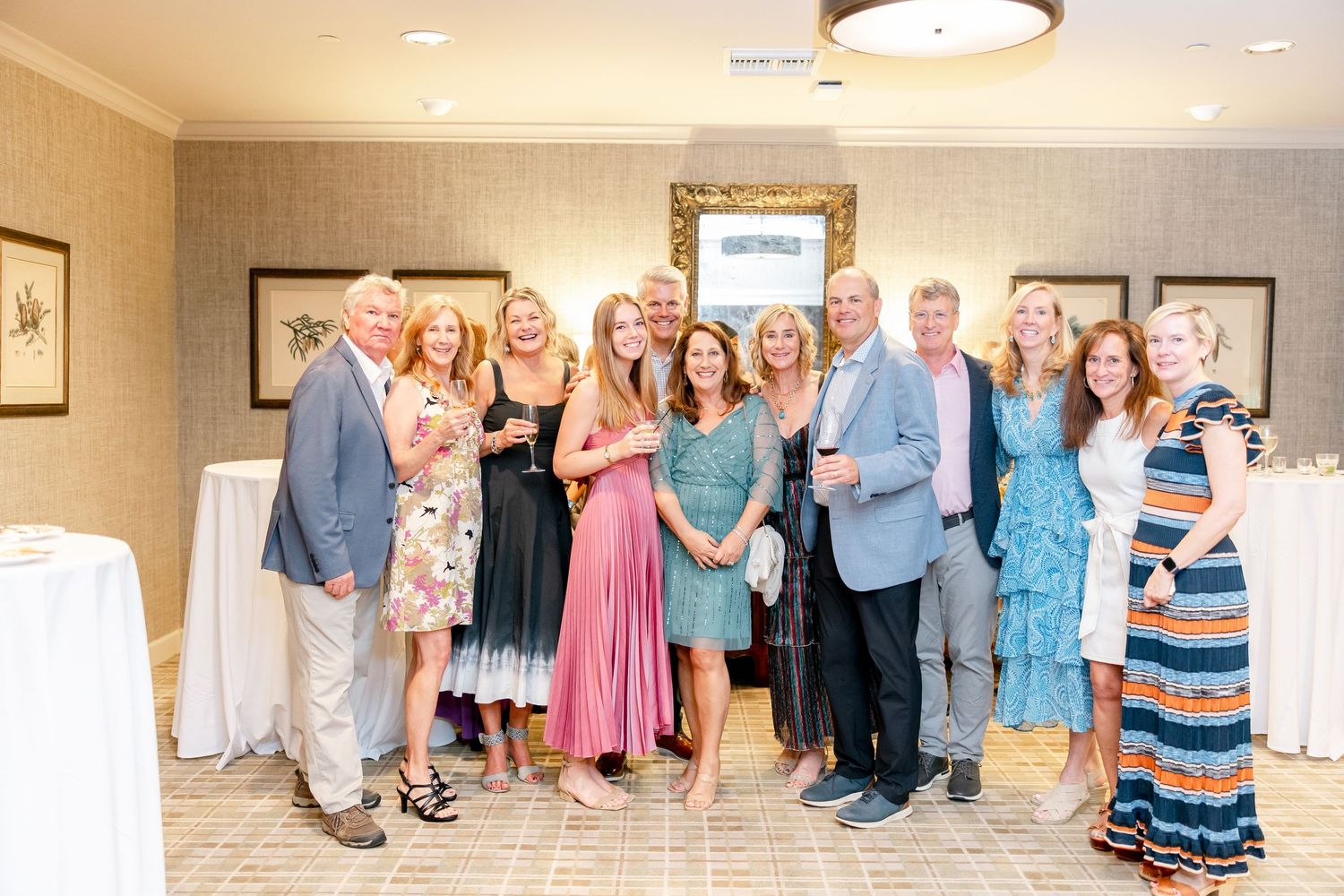 A group in formal attire poses together at an elegant indoor event space with framed artwork on the walls.