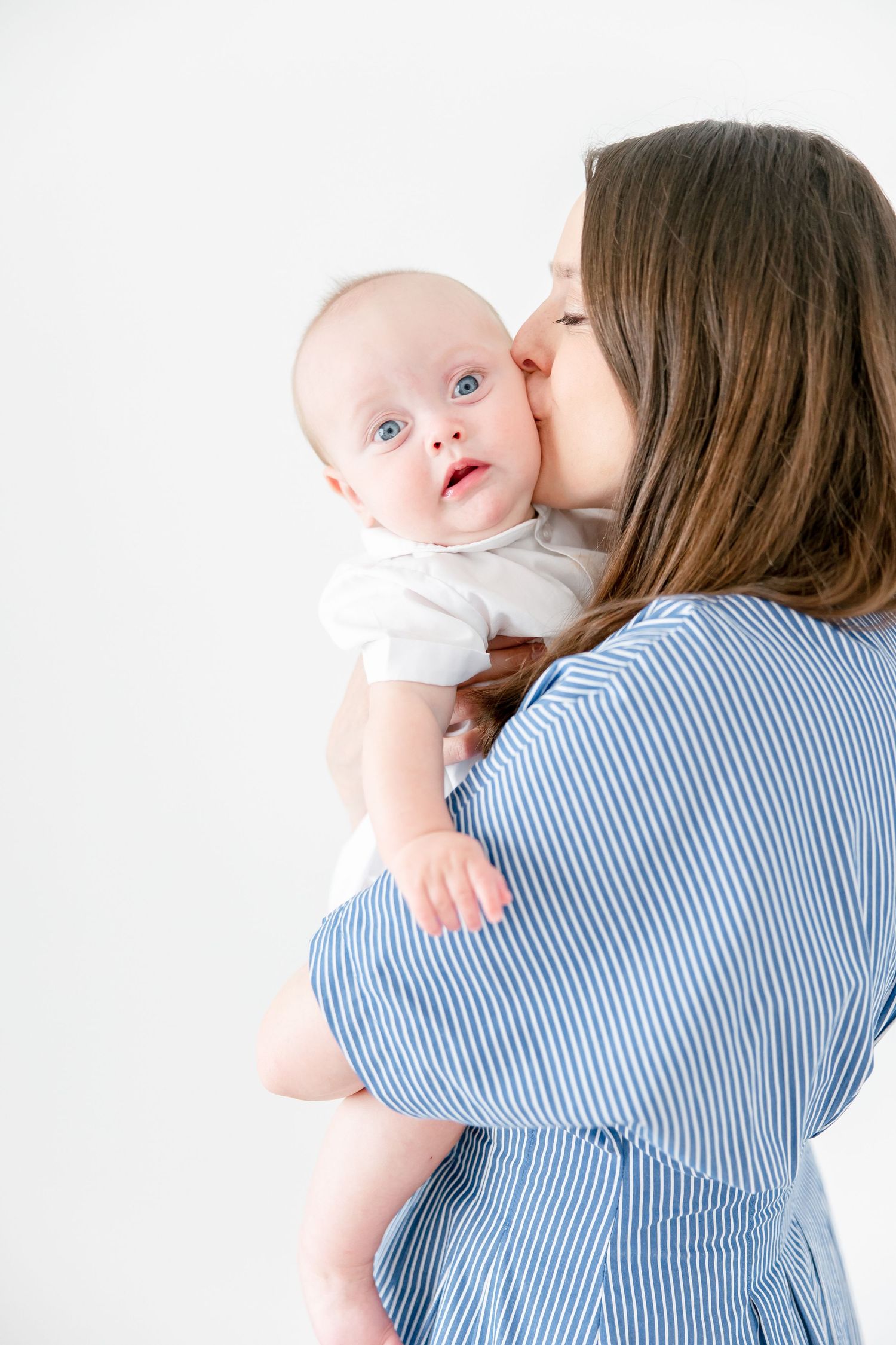 An intimate moment showing affection between a baby in white and someone wearing a blue striped top.