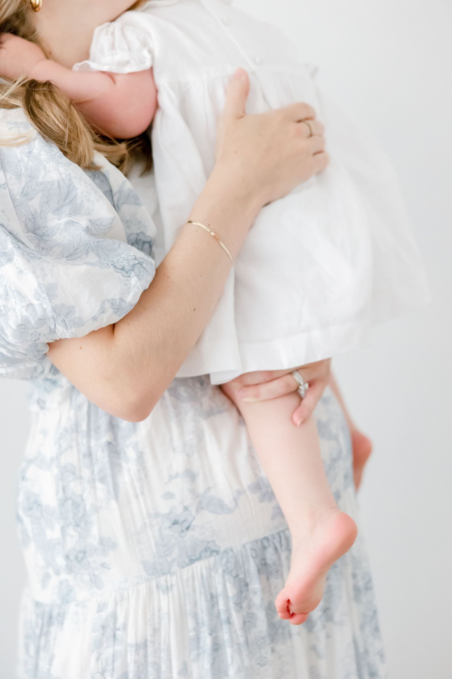 A close up view showing small feet and delicate hands during a tender moment wearing a blue floral dress.