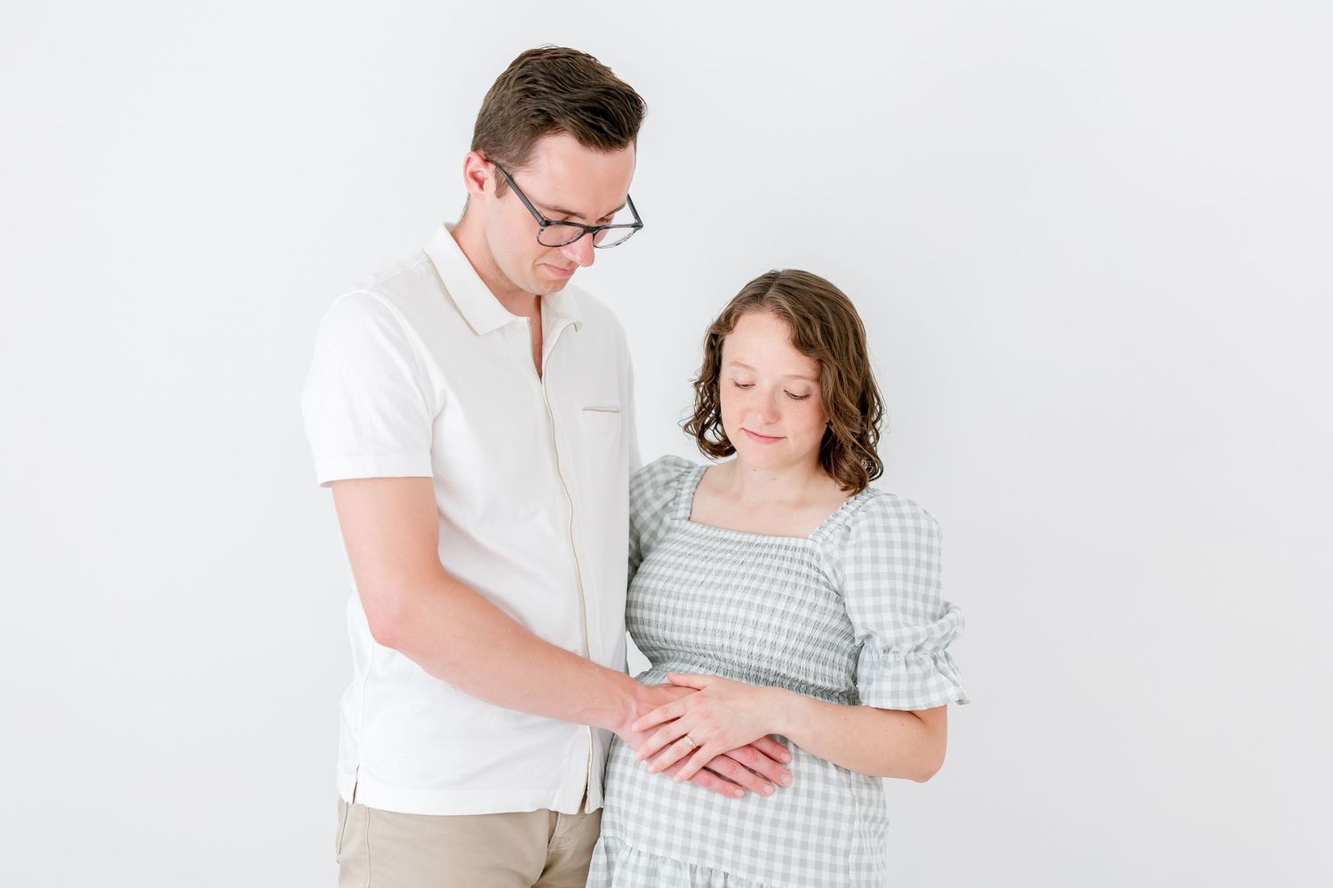 Expecting couple in white and gray outfits pose together during a bright and airy maternity photo session.