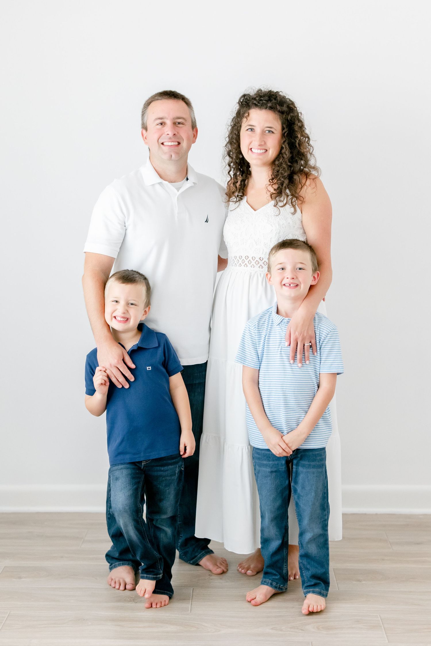 Family poses together in coordinated casual outfits against minimalist white studio background.
