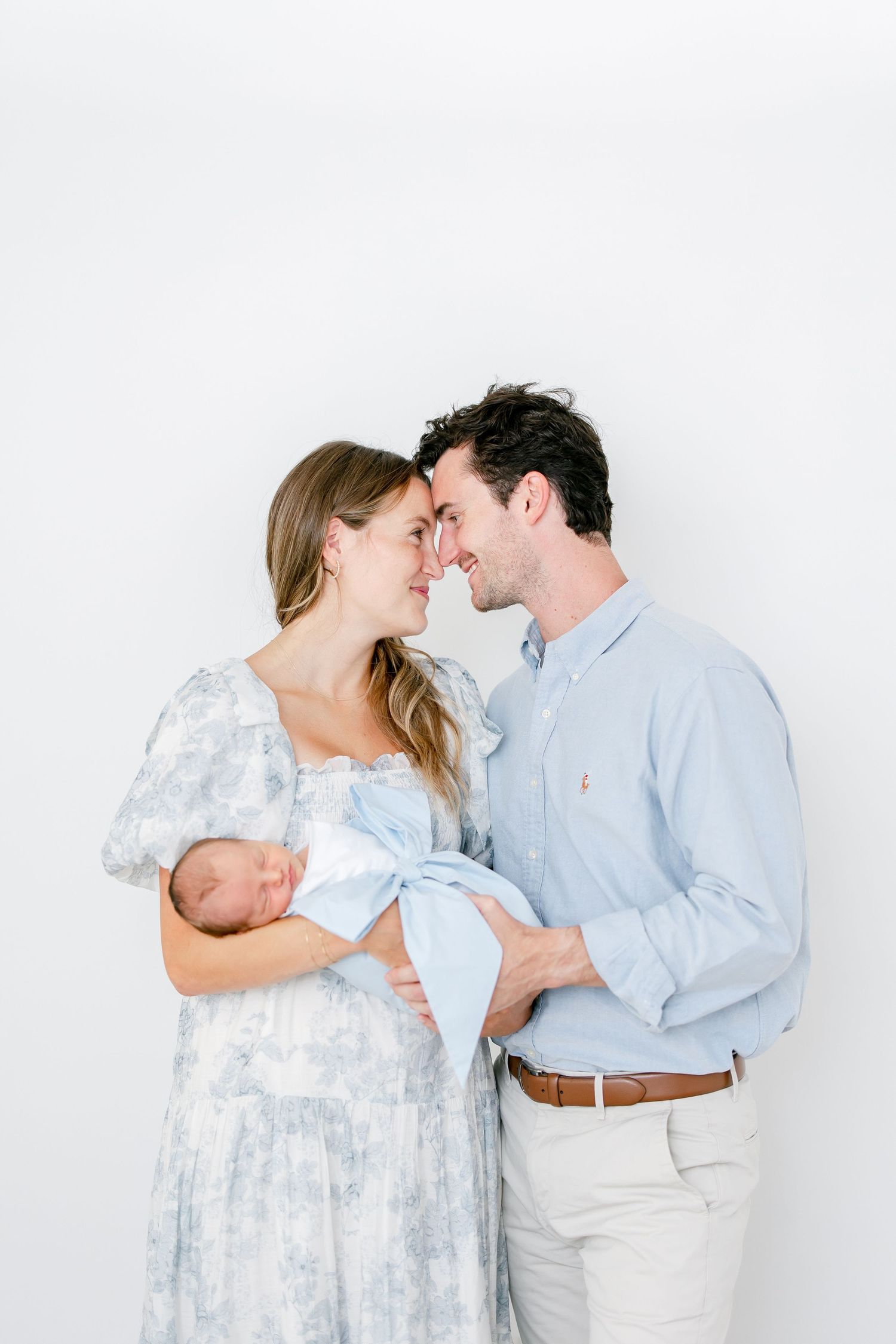 Family in matching light blue and white outfits share intimate moments against a white studio backdrop.