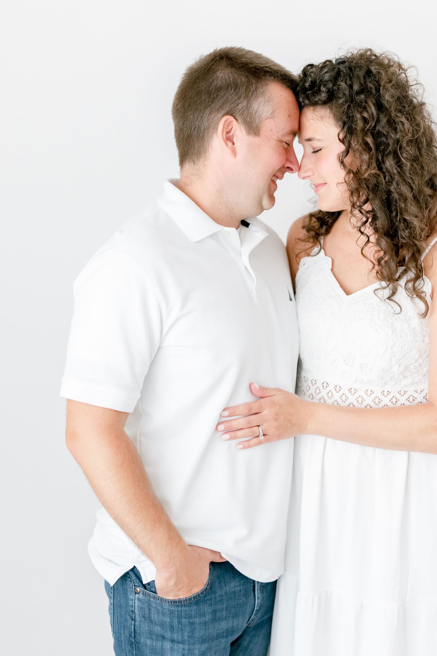 Intimate portrait of couple in white sharing tender moments against minimal white background.