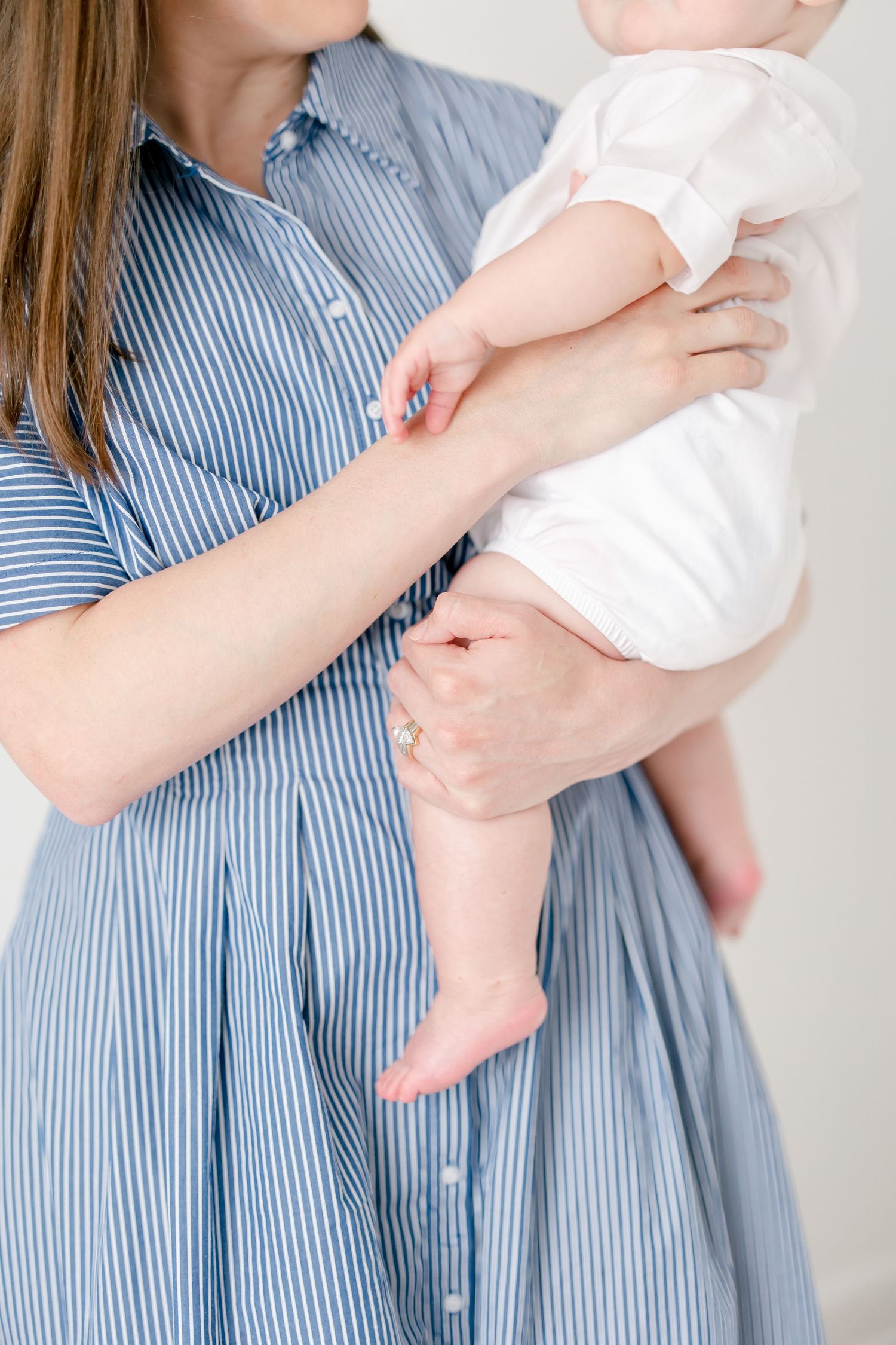 Close-up of small baby feet and hands while being held by someone in a blue striped dress.
