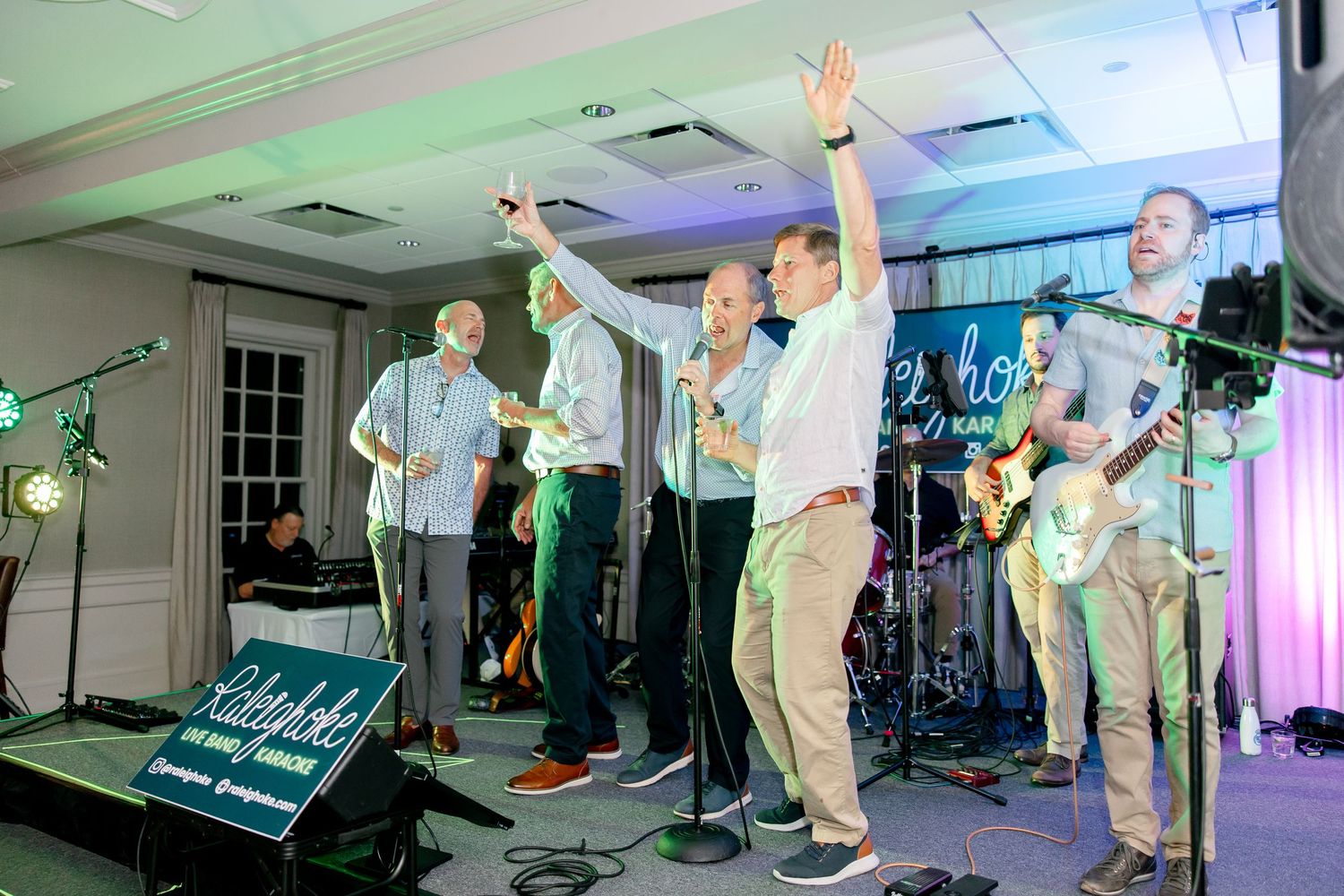Band members perform on stage with raised arms during an energetic live performance with colorful lighting.
