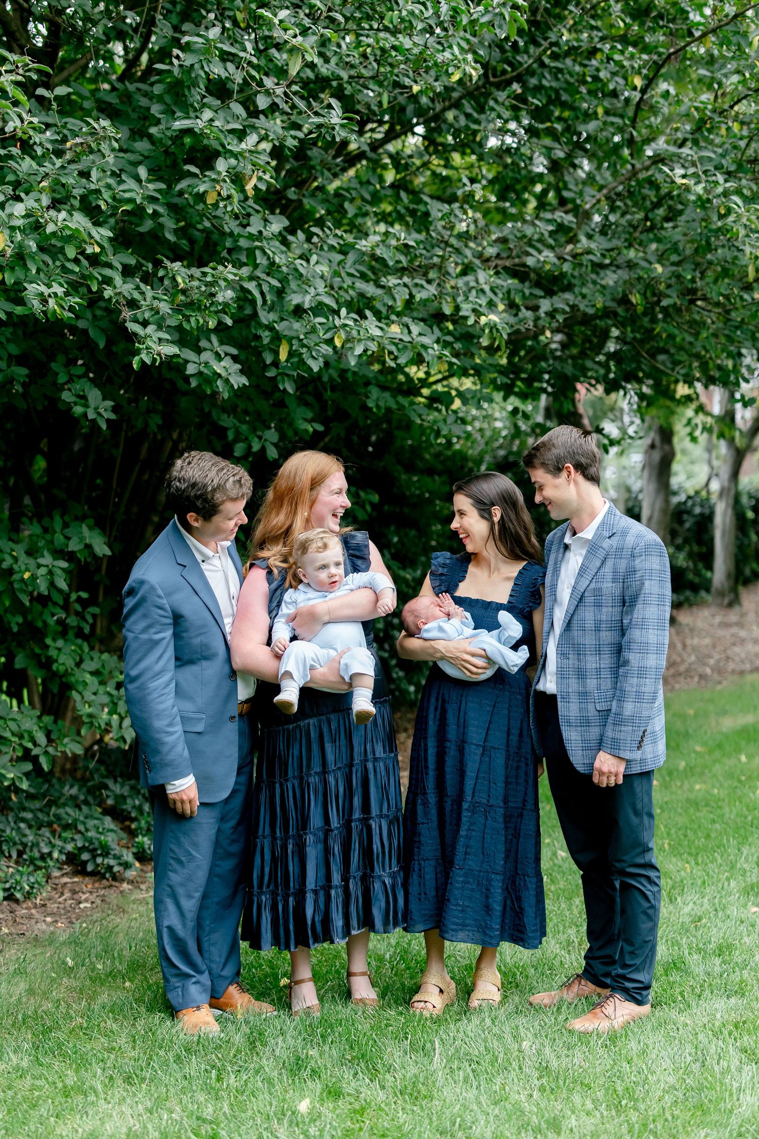 A social gathering outdoors with people wearing coordinated navy blue and gray attire under shady trees.