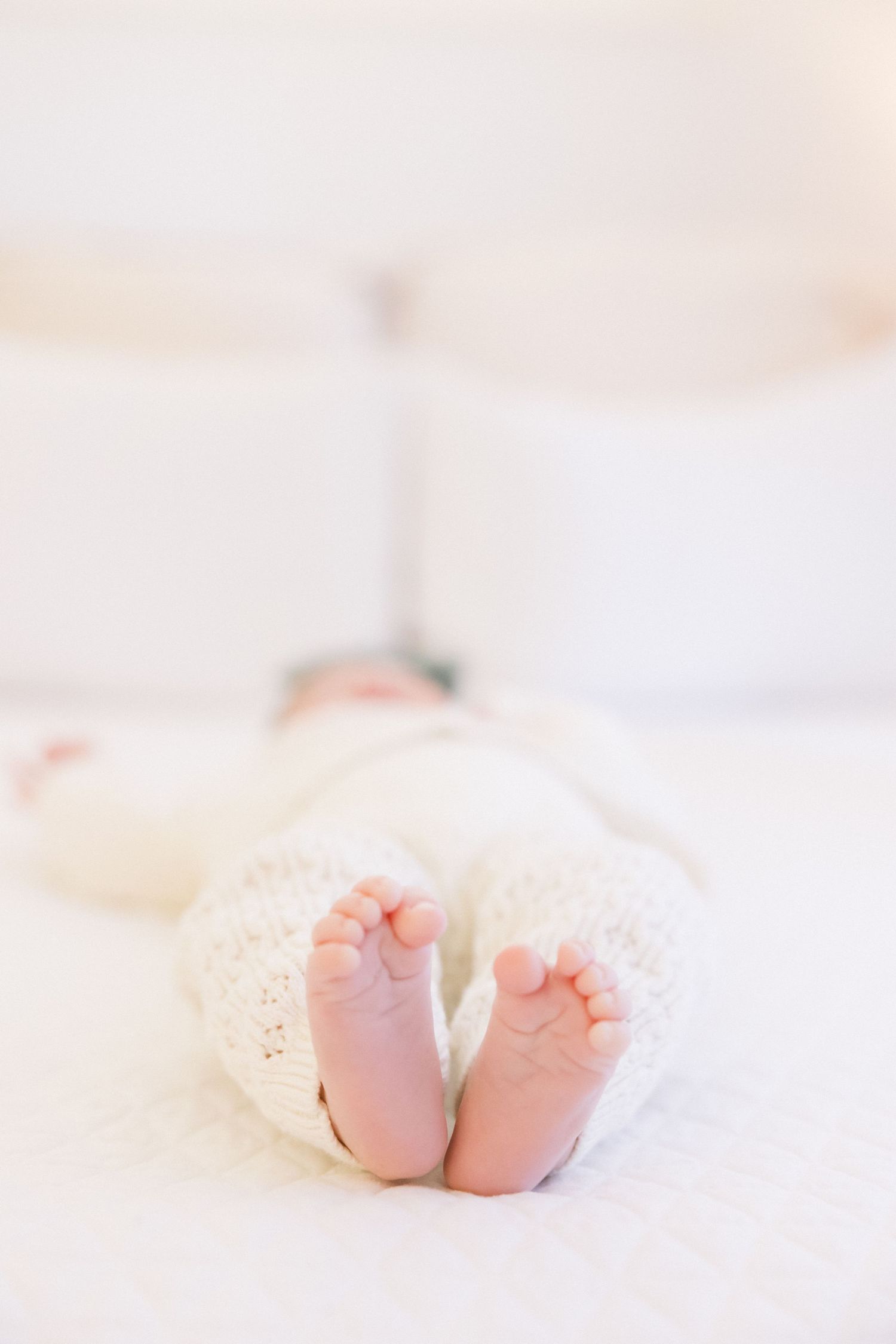 Tiny newborn baby feet peeking out from white blankets on a soft bed.