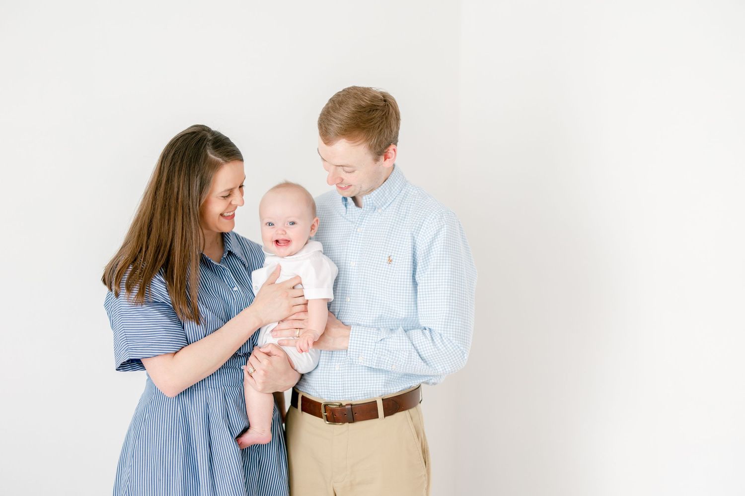 Family portrait of parents in blue shirts with baby against white background.