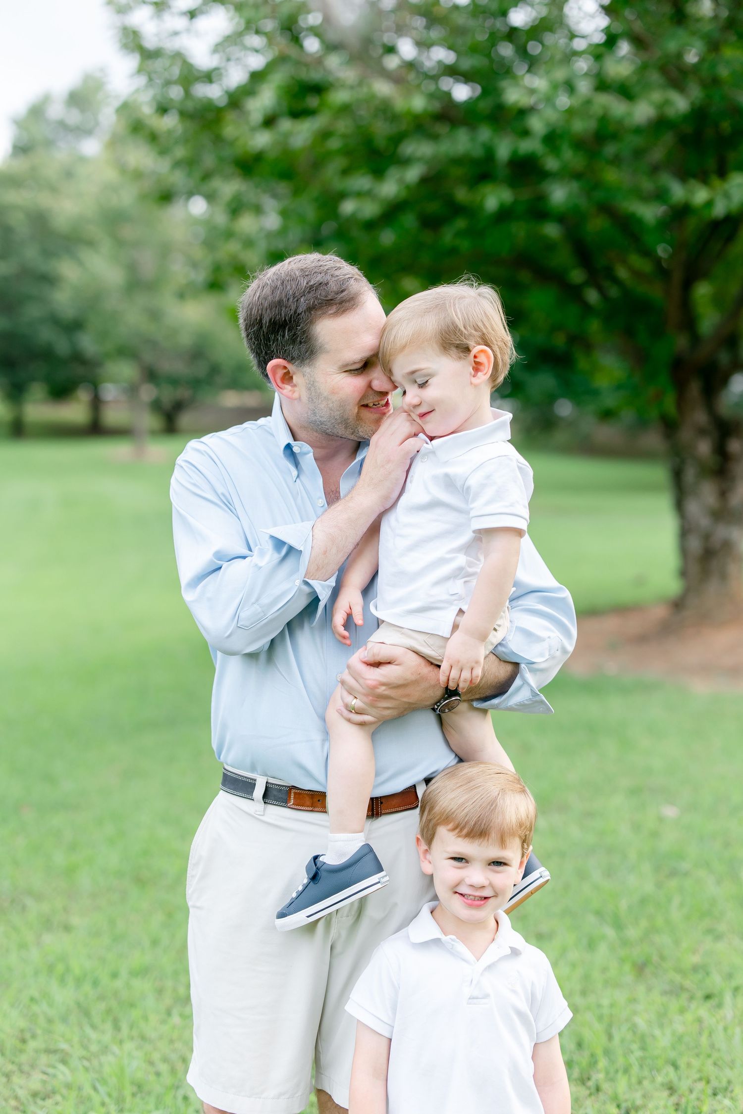 A tender family photo session in a lush green park with matching white and blue outfits.