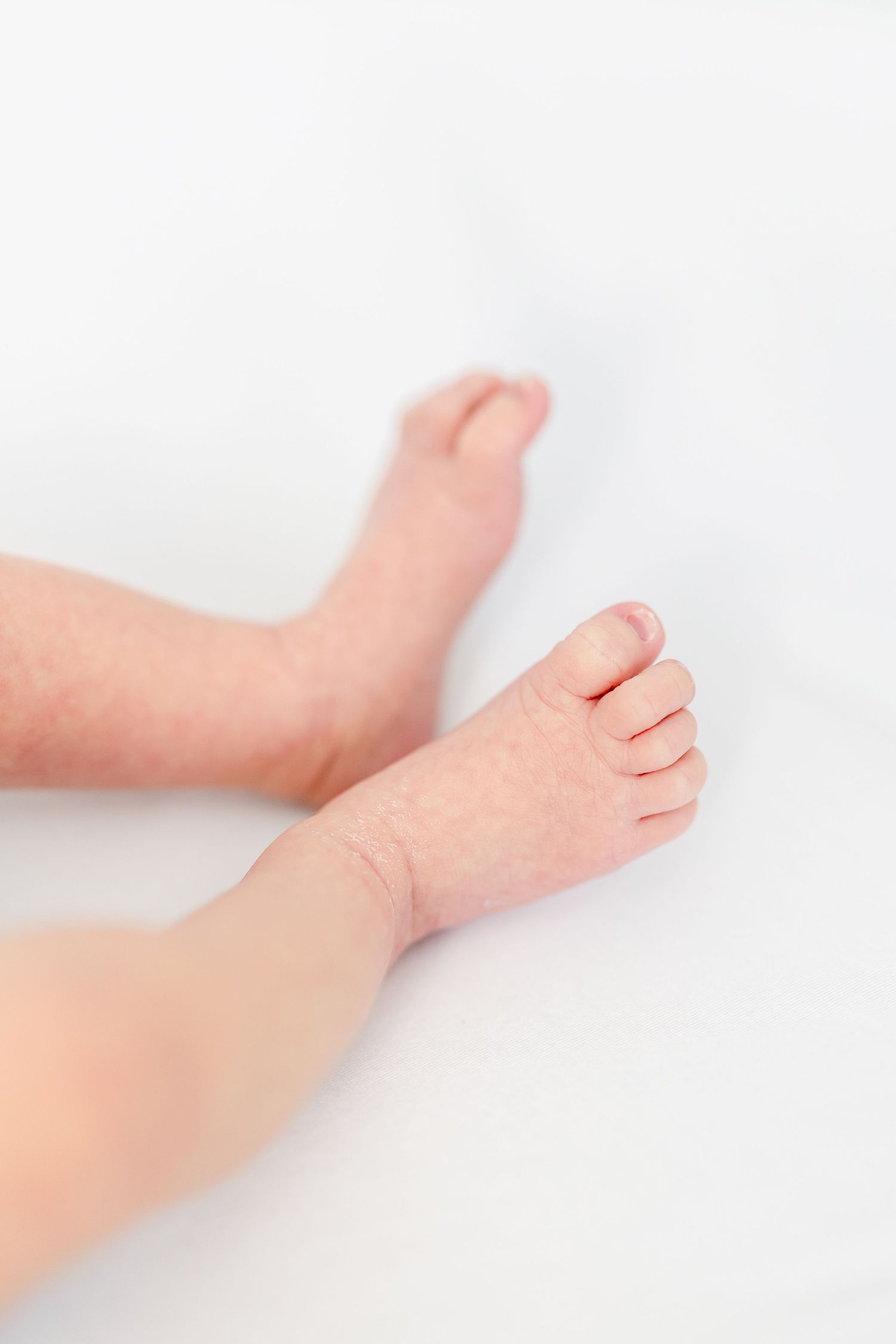 Close-up of tiny newborn baby feet and legs resting on a soft white surface.